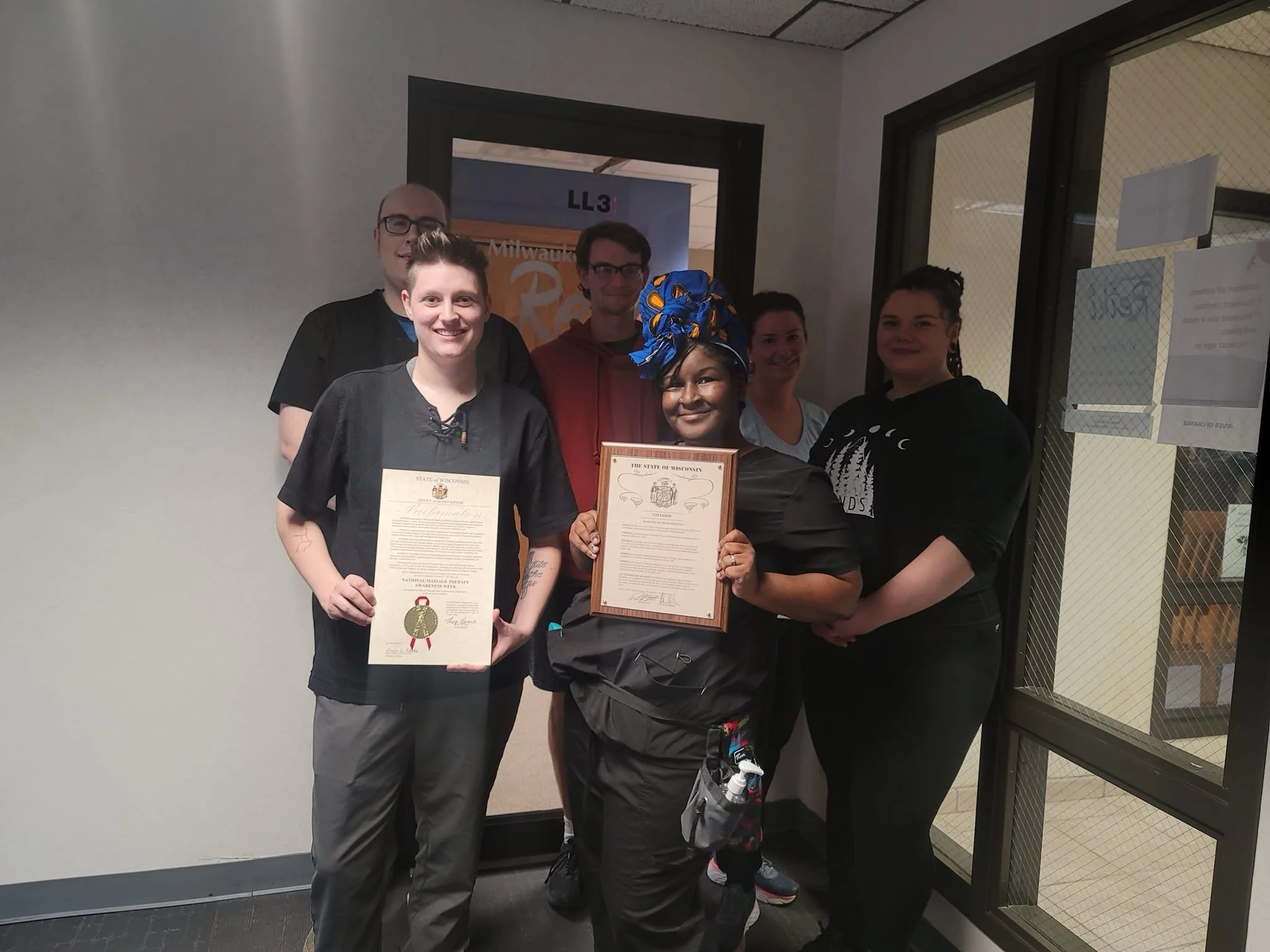 Six people standing together indoors, holding certificates, with one person wearing a headwrap, smiling at the camera.