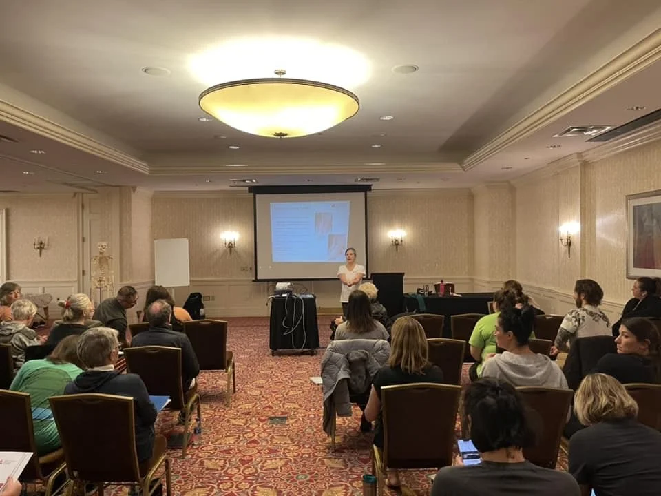 A woman giving a presentation in a conference room with seated audience.