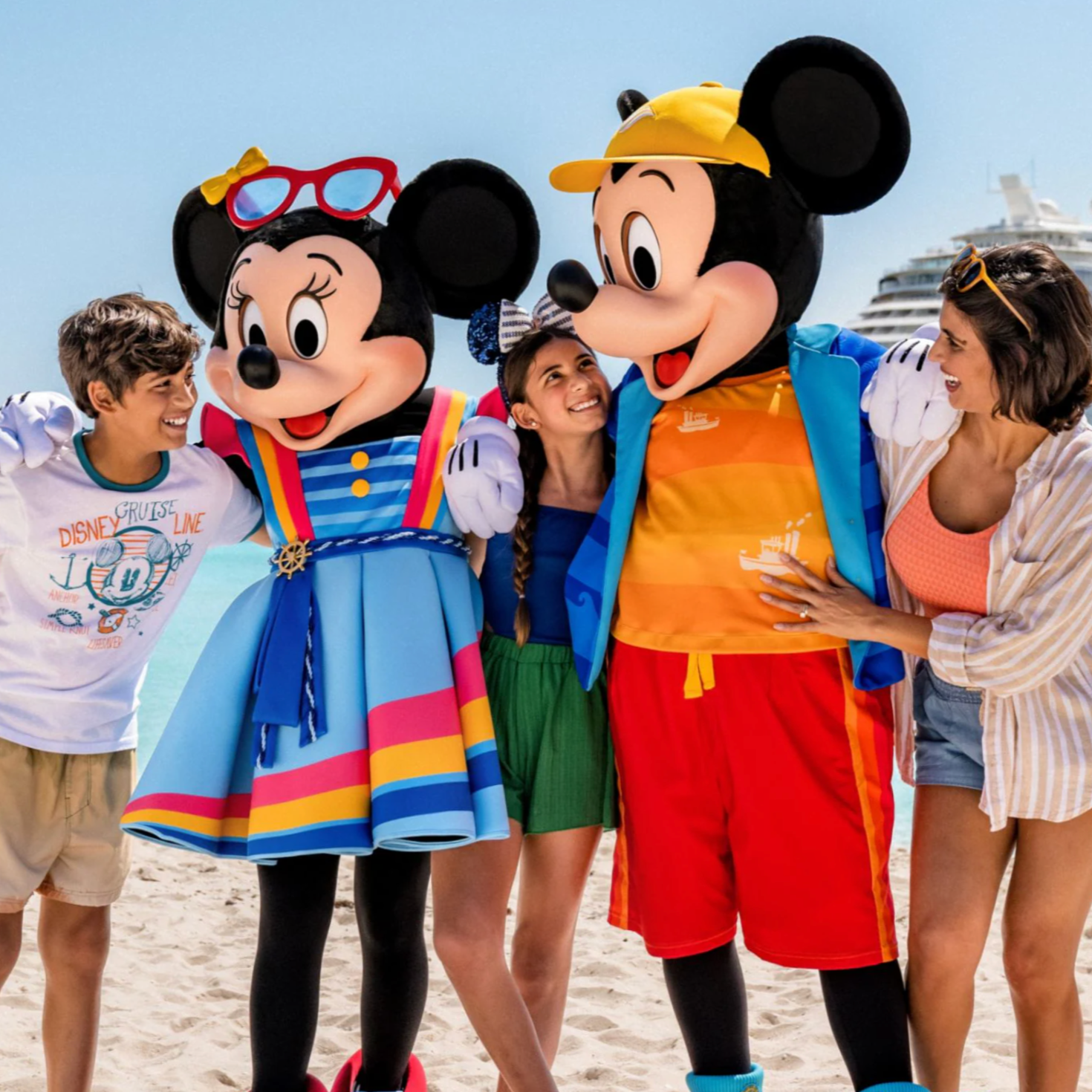 People on a beach with Minnie Mouse and Mickey Mouse mascots, smiling and posing for a photo.