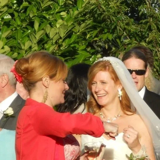 People celebrating outdoors, with Kate as celebrant talking to the bride who is holding a drink and smiling, surrounded by others.