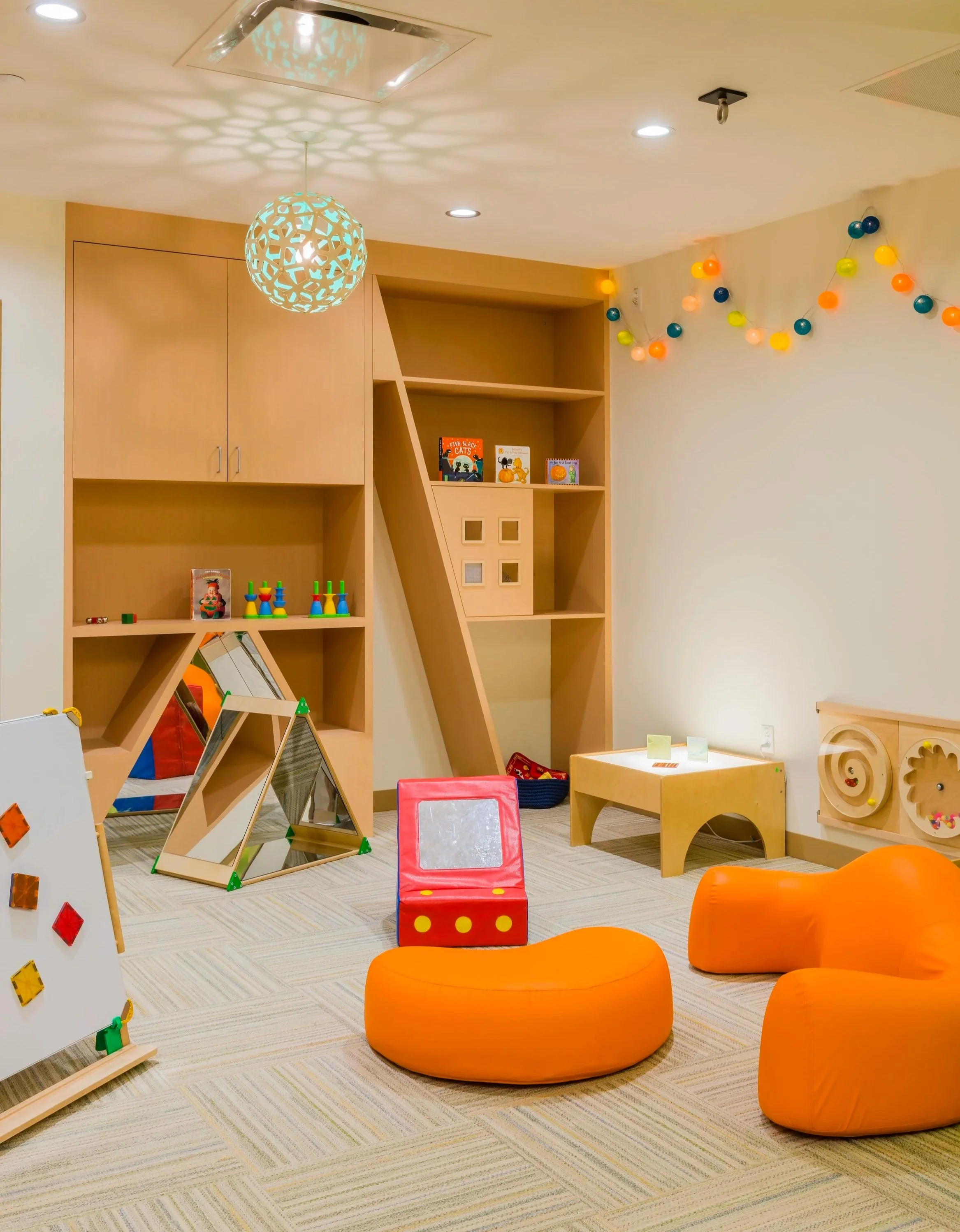 Children’s sensory room with soft orange seating, interactive wall features, mirrors, built-in shelving, and colorful lighting.