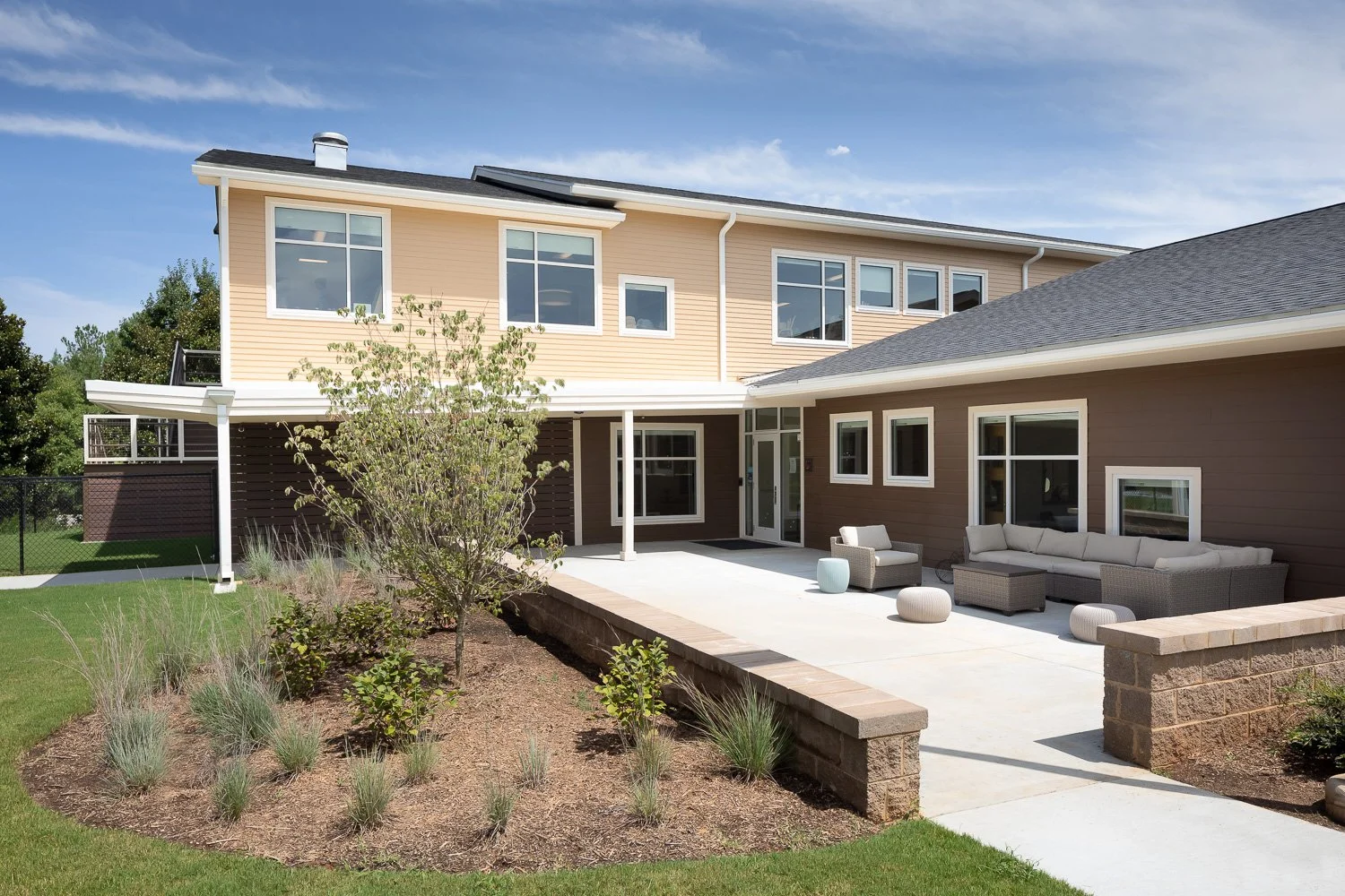 Exterior courtyard of an early learning center with landscaped gardens, lawn, patio seating, and direct access to the building.