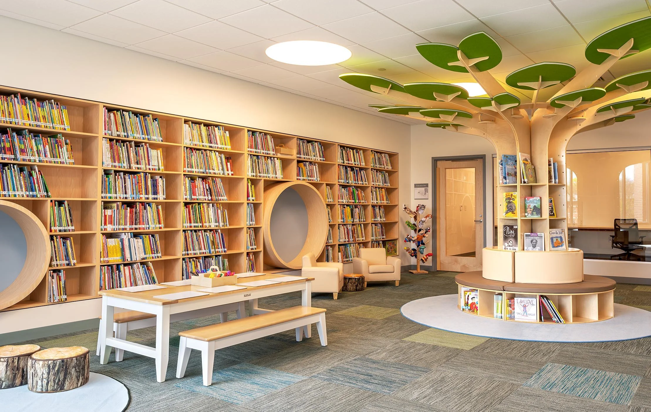 Children’s library with built-in bookshelves, circular reading nooks, child-sized furnishings, and a tree-inspired centerpiece with integrated book displays.