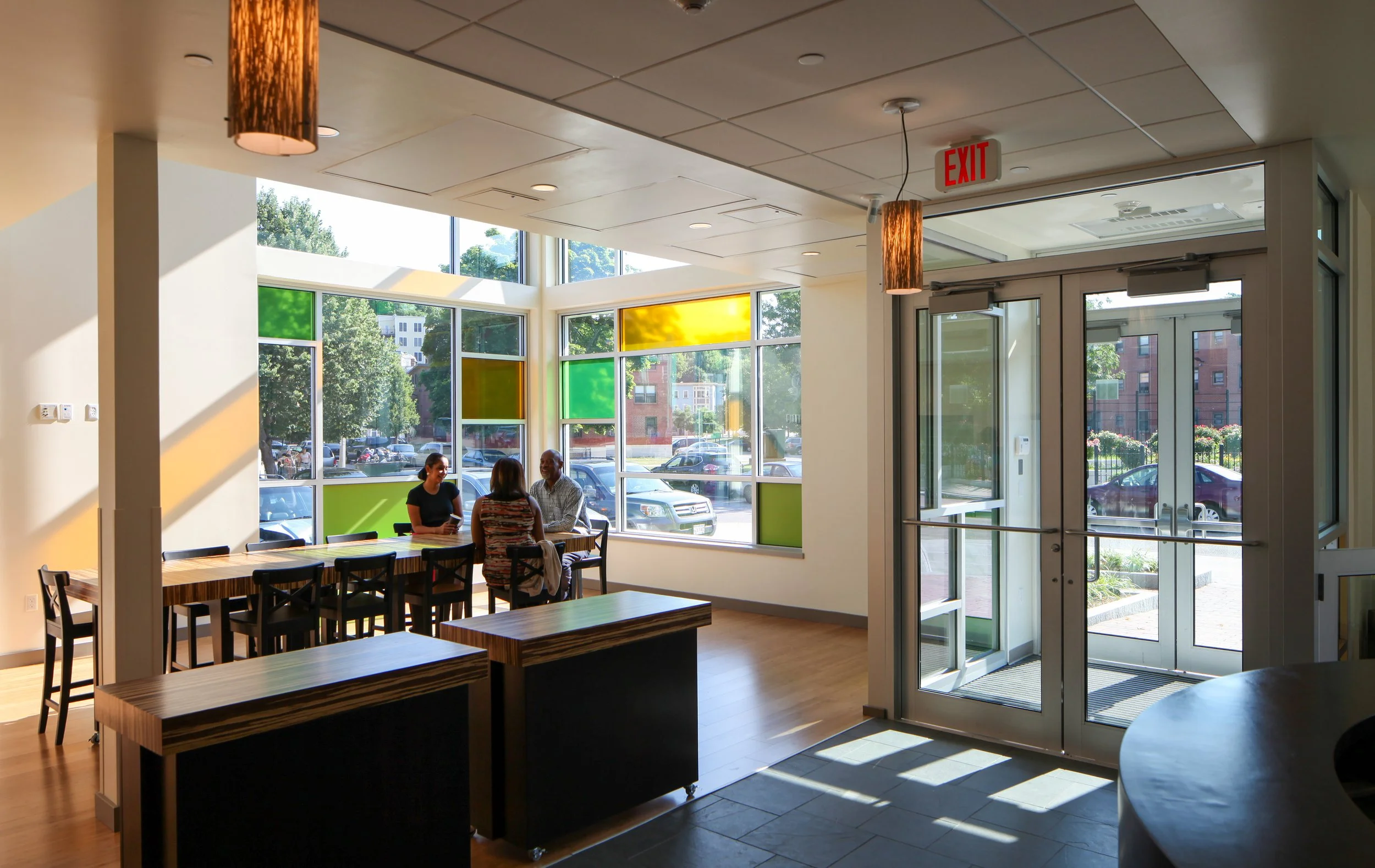 Sunlit entrance and gathering area at Nurtury Learning Lab with colorful windows, flexible tables, and seating.