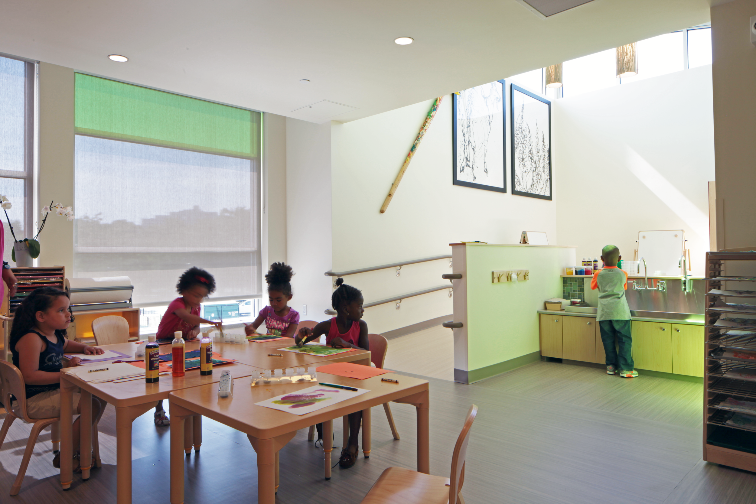 Children creating art in a bright classroom with child-sized tables, sinks, and abundant natural light.