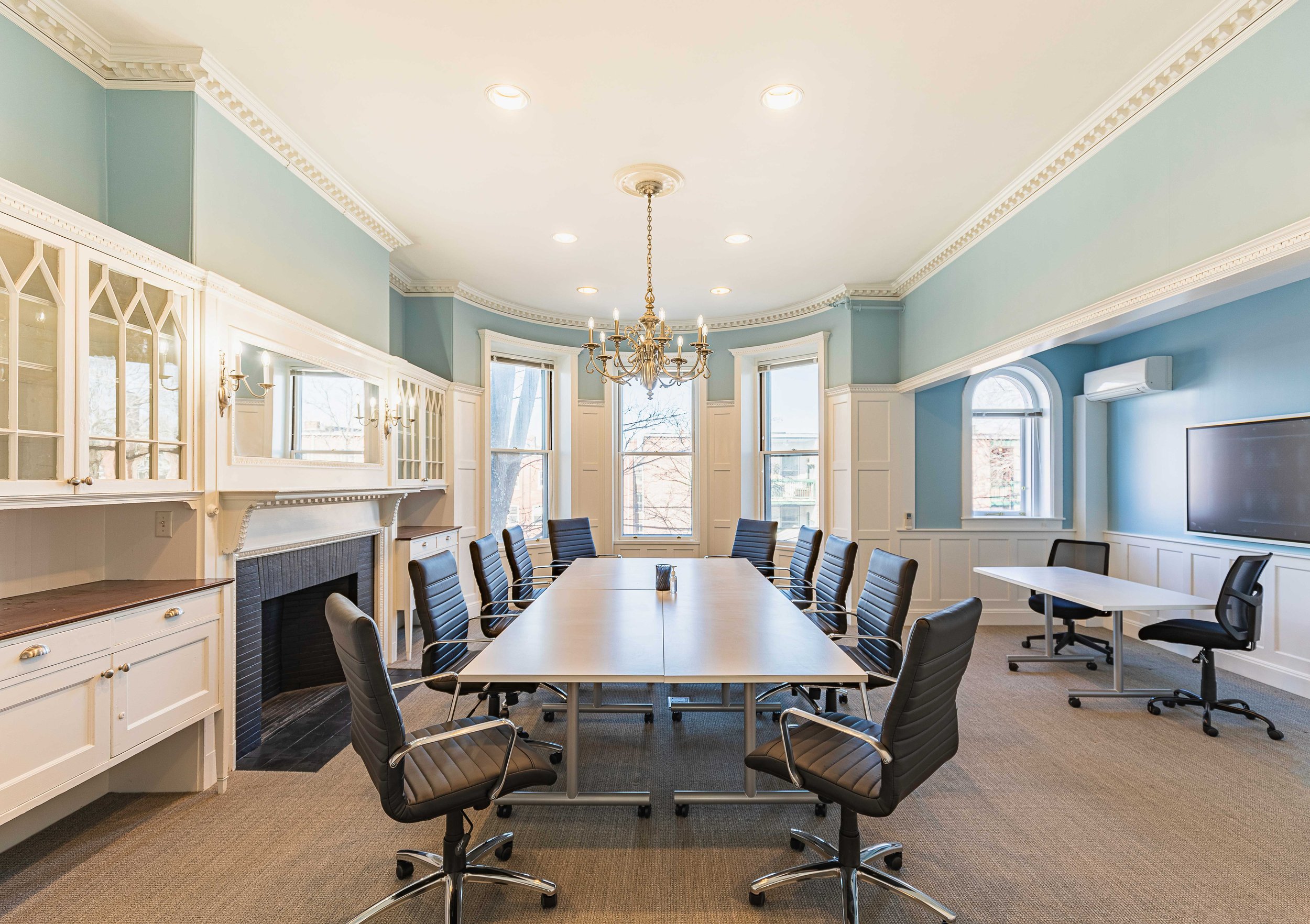 Conference room with a long meeting table, flexible seating, built-in cabinetry, fireplace, large windows, and wall-mounted display.