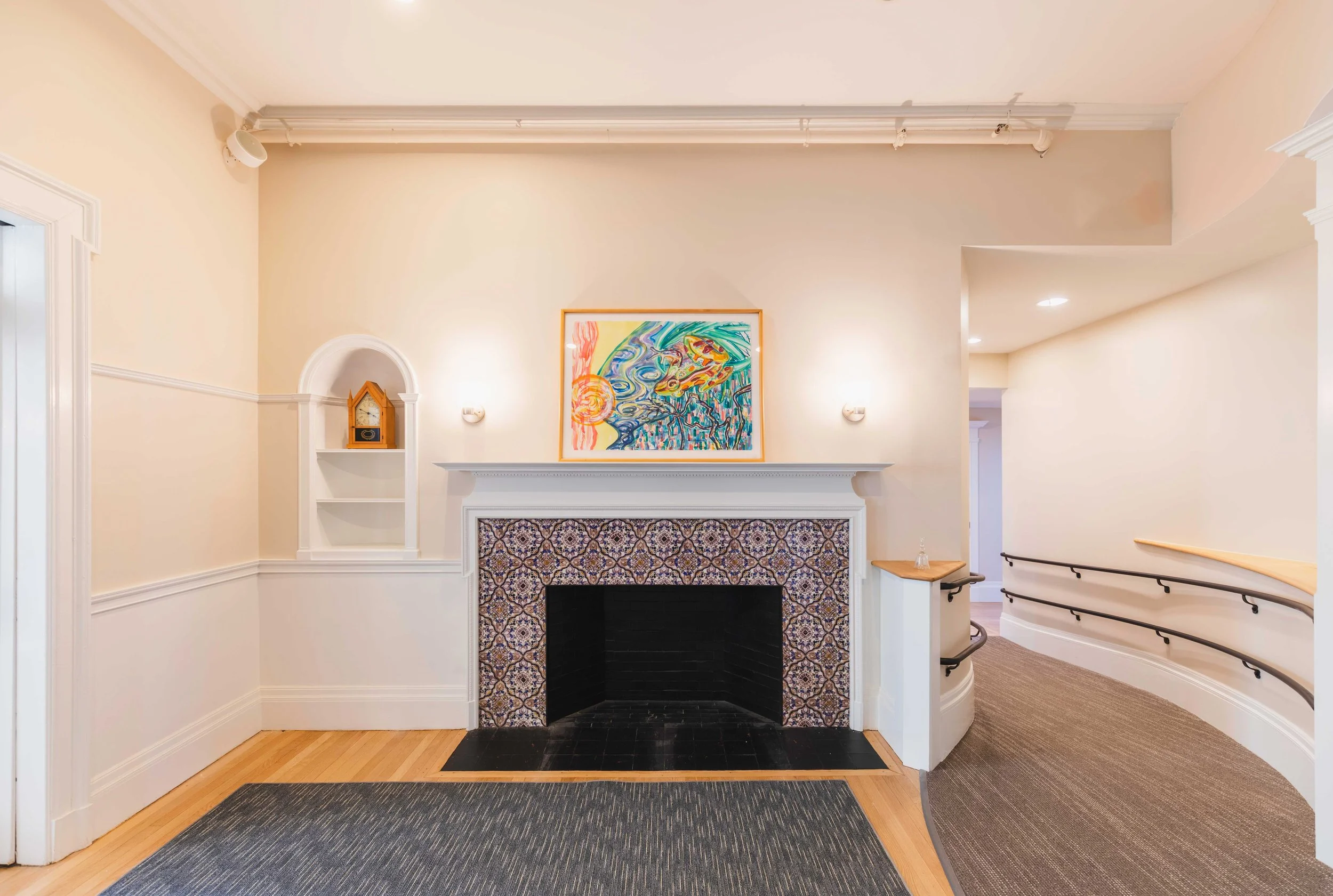 Interior space featuring a decorative tiled fireplace, artwork, wood flooring, and a curved corridor with handrails.