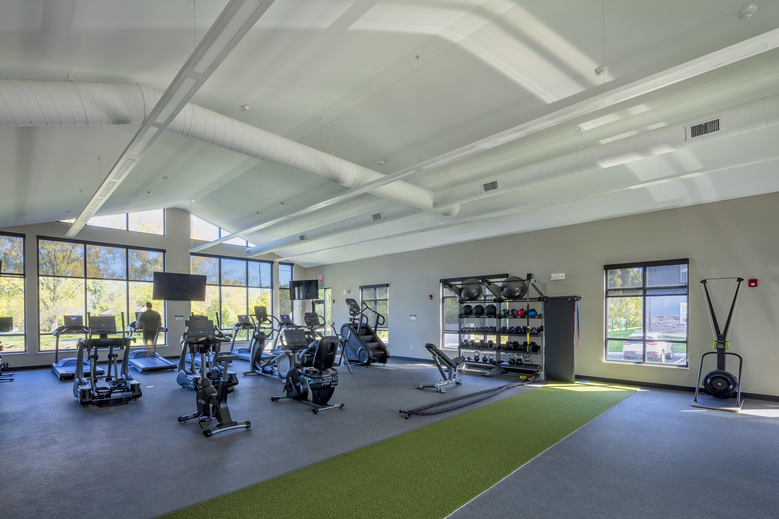 Fitness center with cardio equipment, free weights, strength training equipment, and open exercise space illuminated by large windows.
