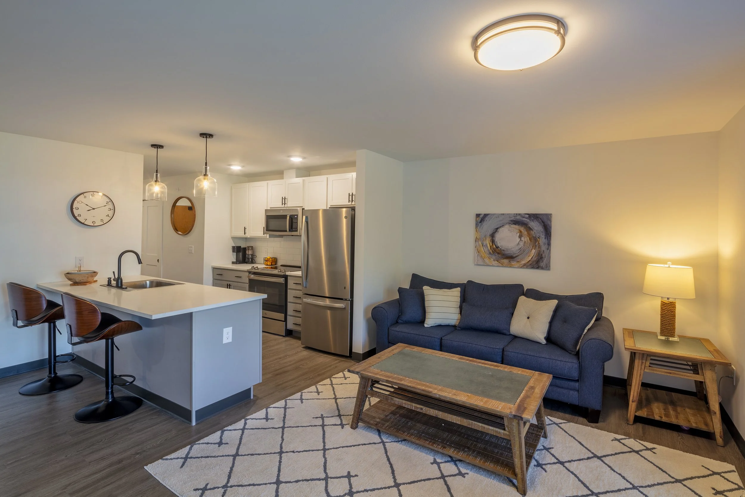 Open-concept apartment featuring a kitchen with island seating, stainless steel appliances, dining area, and living room with sofa and coffee table.