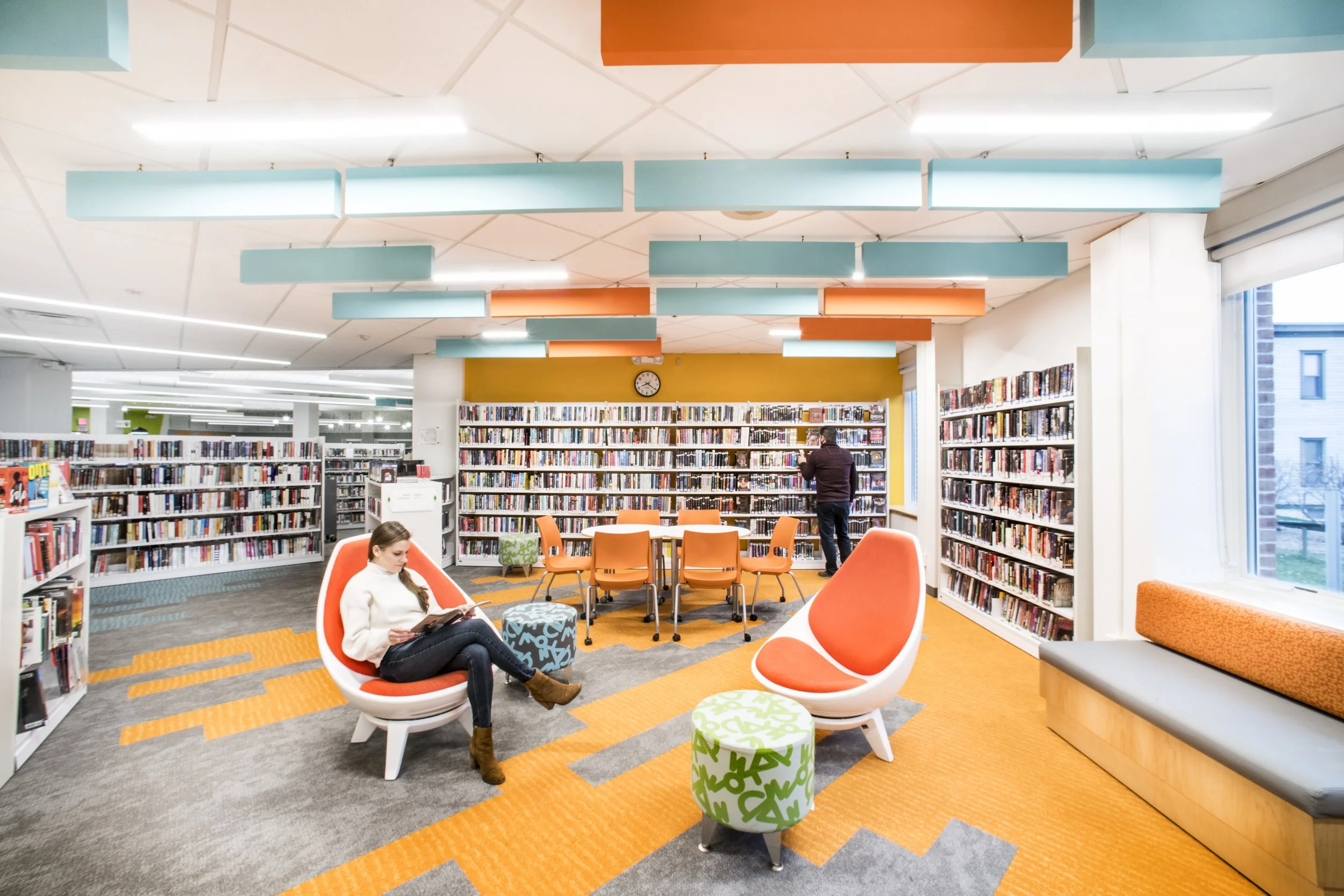 Colorful library interior with bookshelves, modern lounge seating, study tables, and suspended acoustic panels.