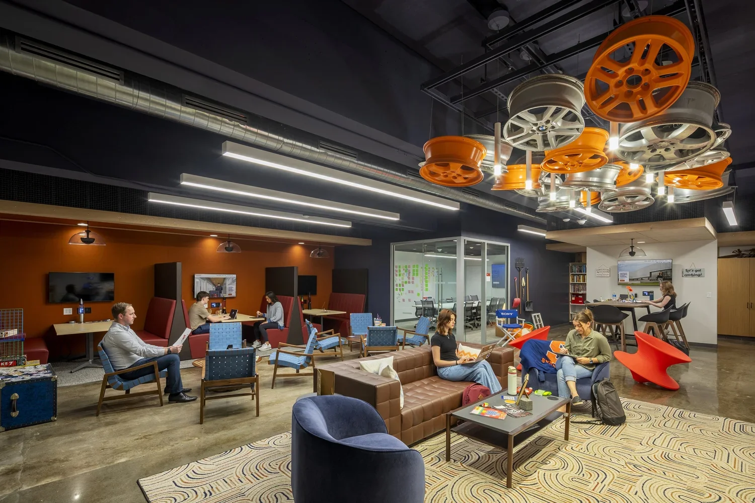 Collaborative student lounge with flexible seating, study booths, meeting spaces, and a suspended ceiling feature made from colorful automotive wheels.