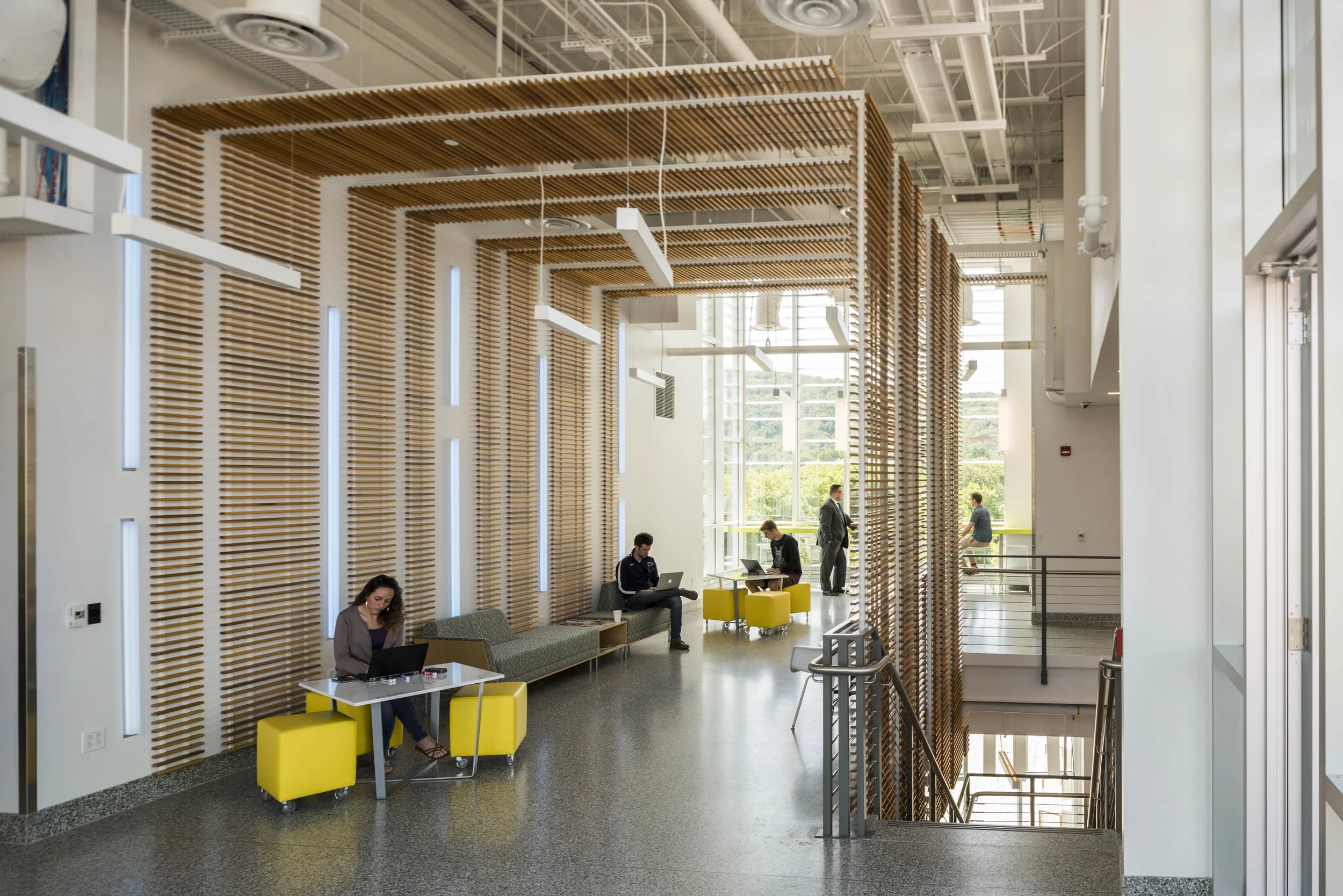 Open collaboration corridor with integrated seating, wood slat architectural features, and informal workspaces that encourage connection and innovation.