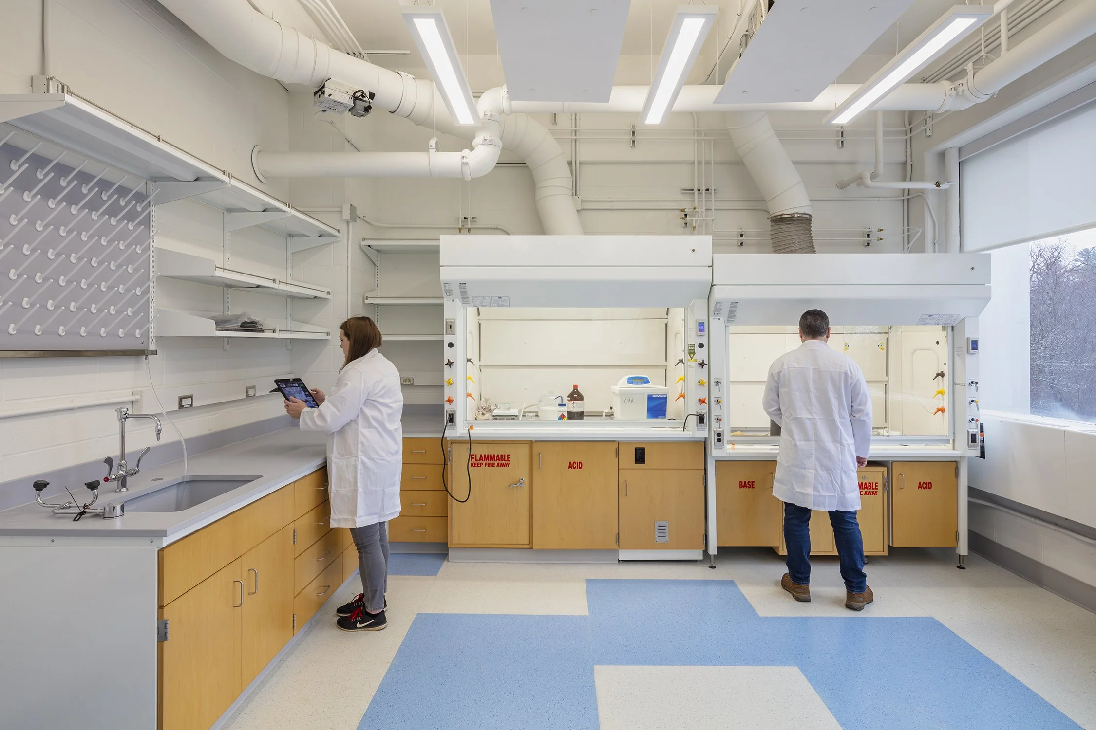 Researchers working in a Cornell University laboratory with chemical fume hoods and laboratory workstations.