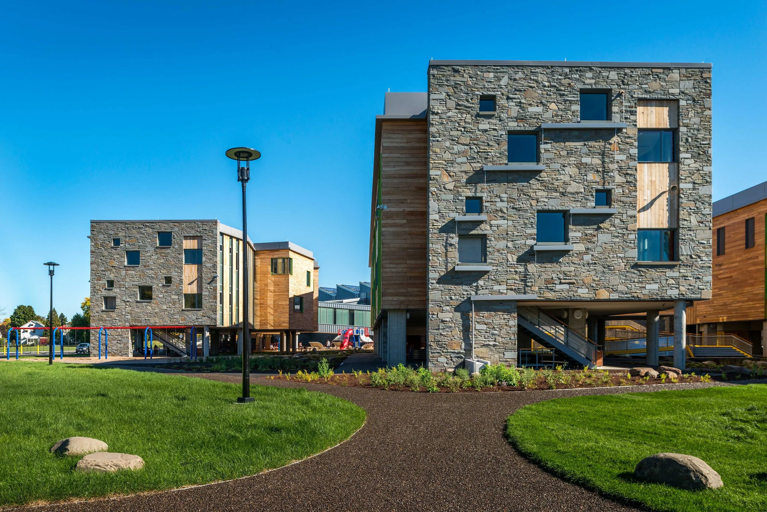 Exterior view highlighting the school’s stone and wood classroom wings elevated above the landscaped site.