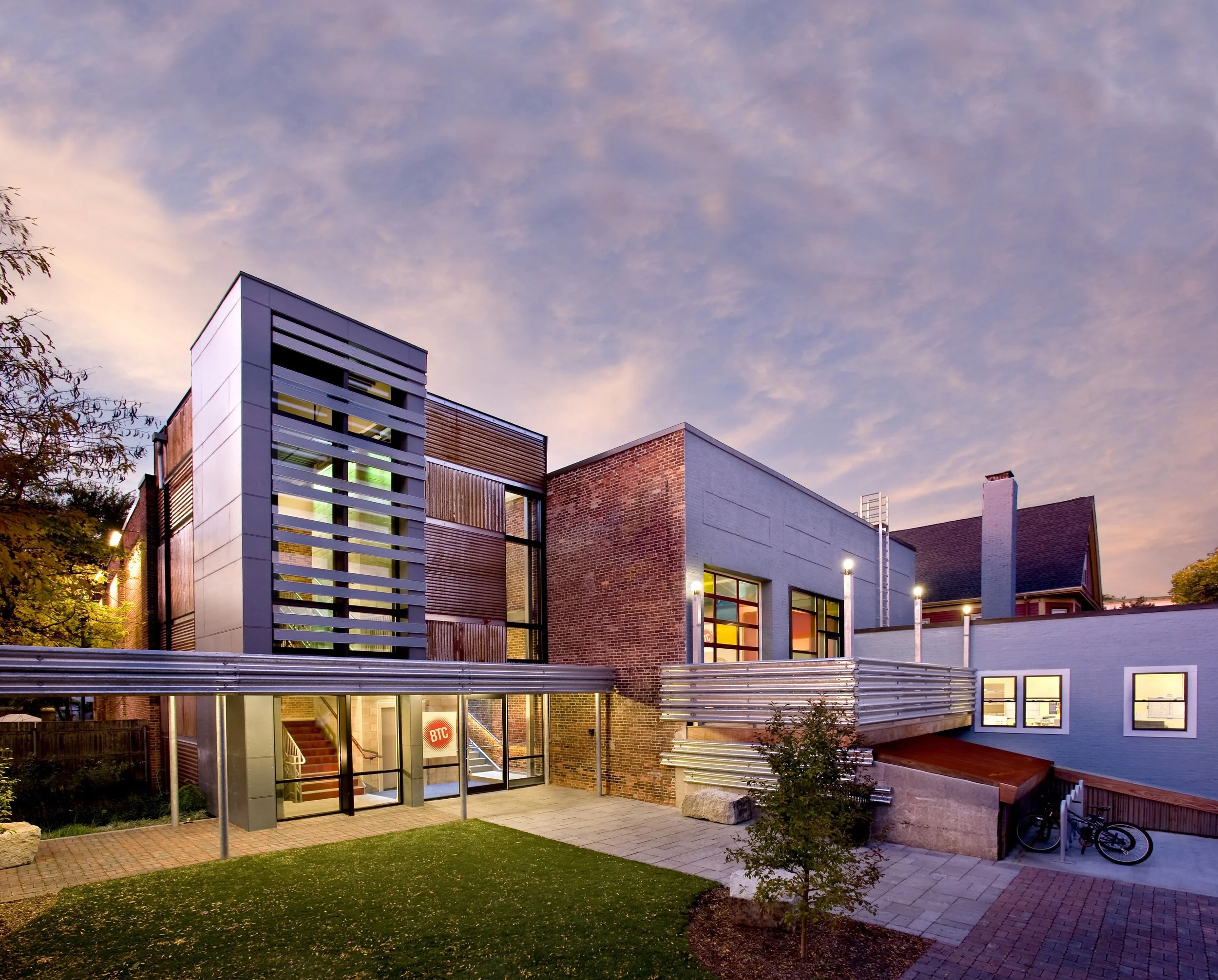 Contemporary community building exterior featuring modern materials, glass entry, landscaped courtyard, and outdoor gathering space.