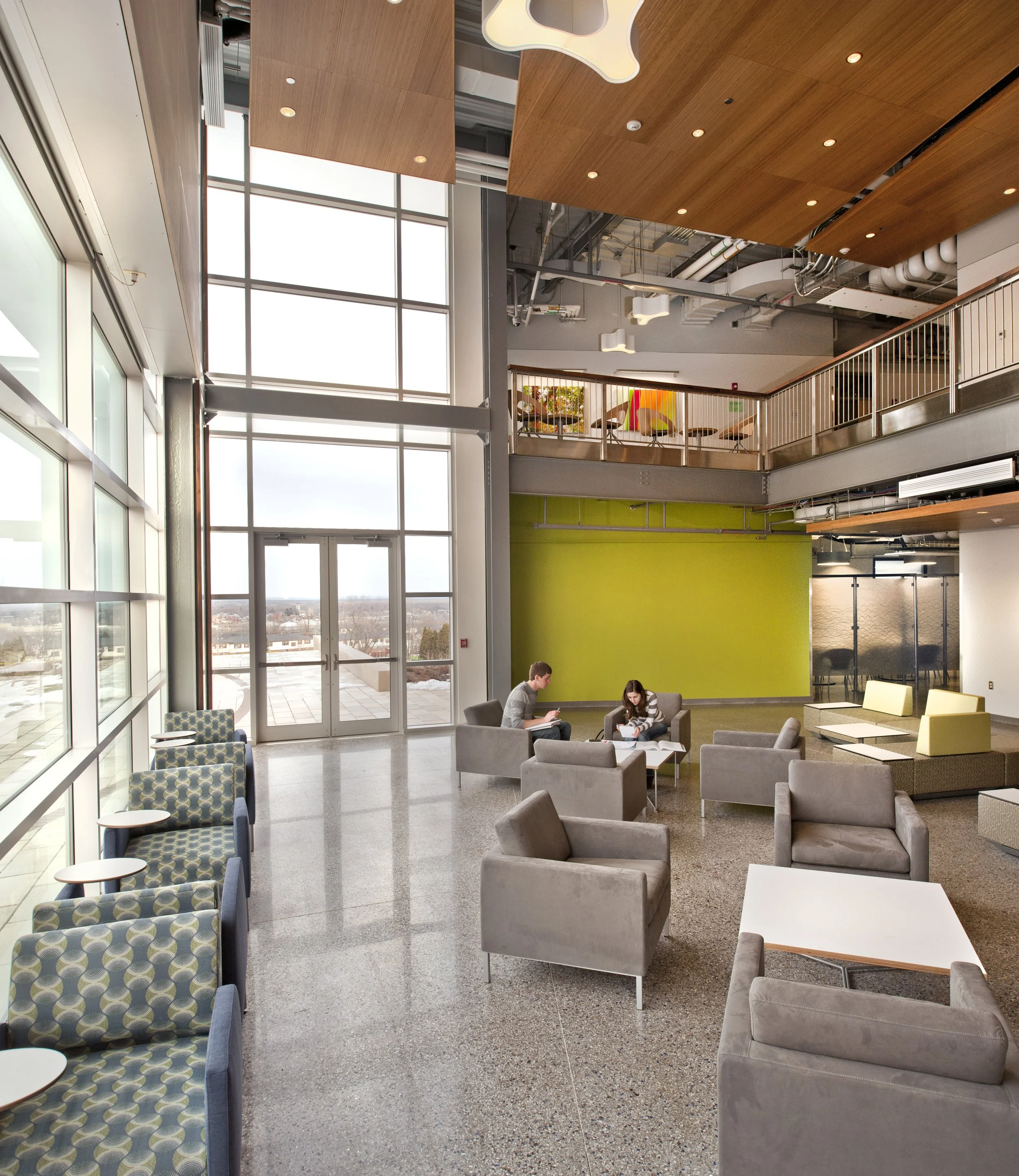Two-story student commons with lounge seating, mezzanine, and daylight-filled gathering space.