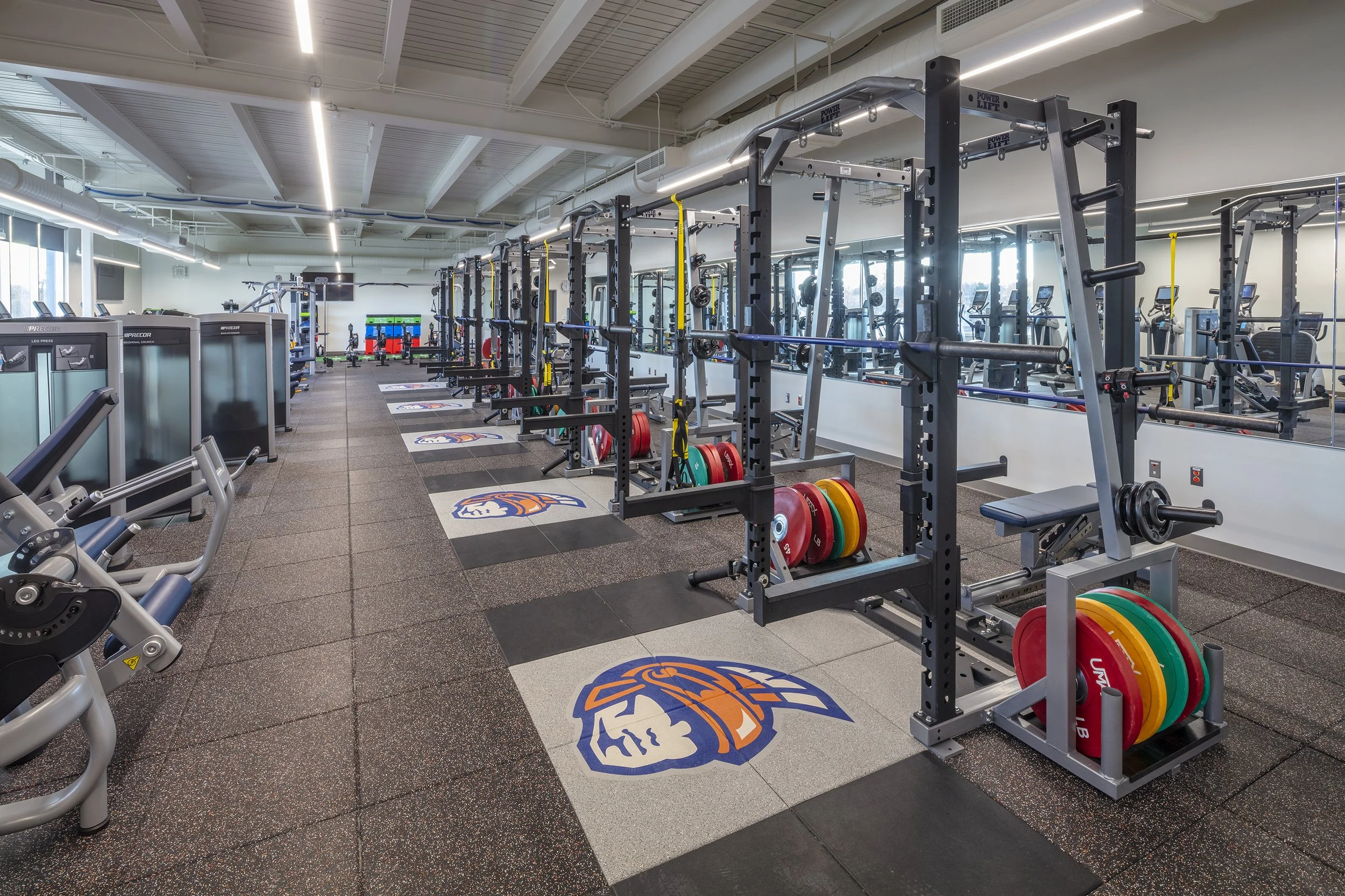 Liverpool High School fitness center with weight racks, strength training equipment, cardio machines, and Warriors branding.