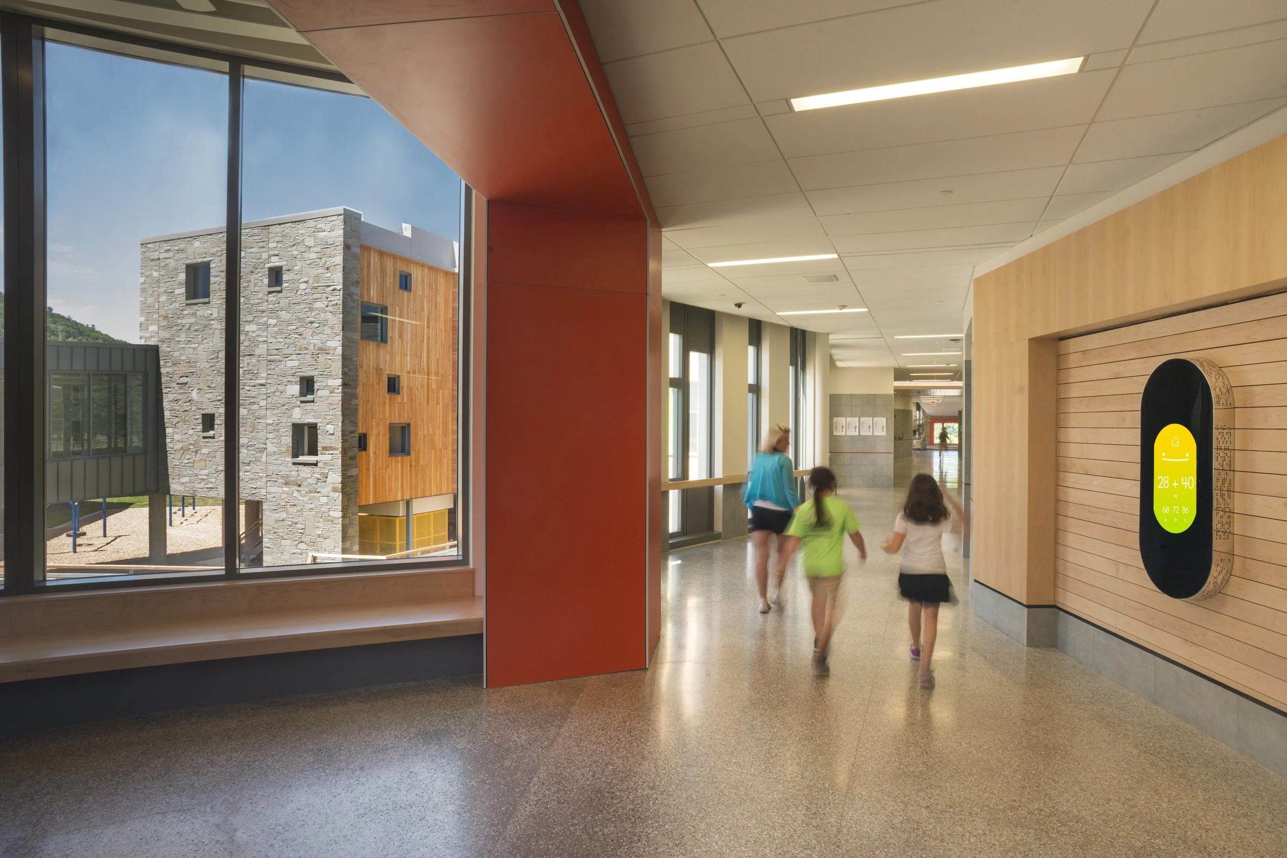 Daylit school corridor with integrated seating, warm wood finishes, and views to the outdoor learning environment.