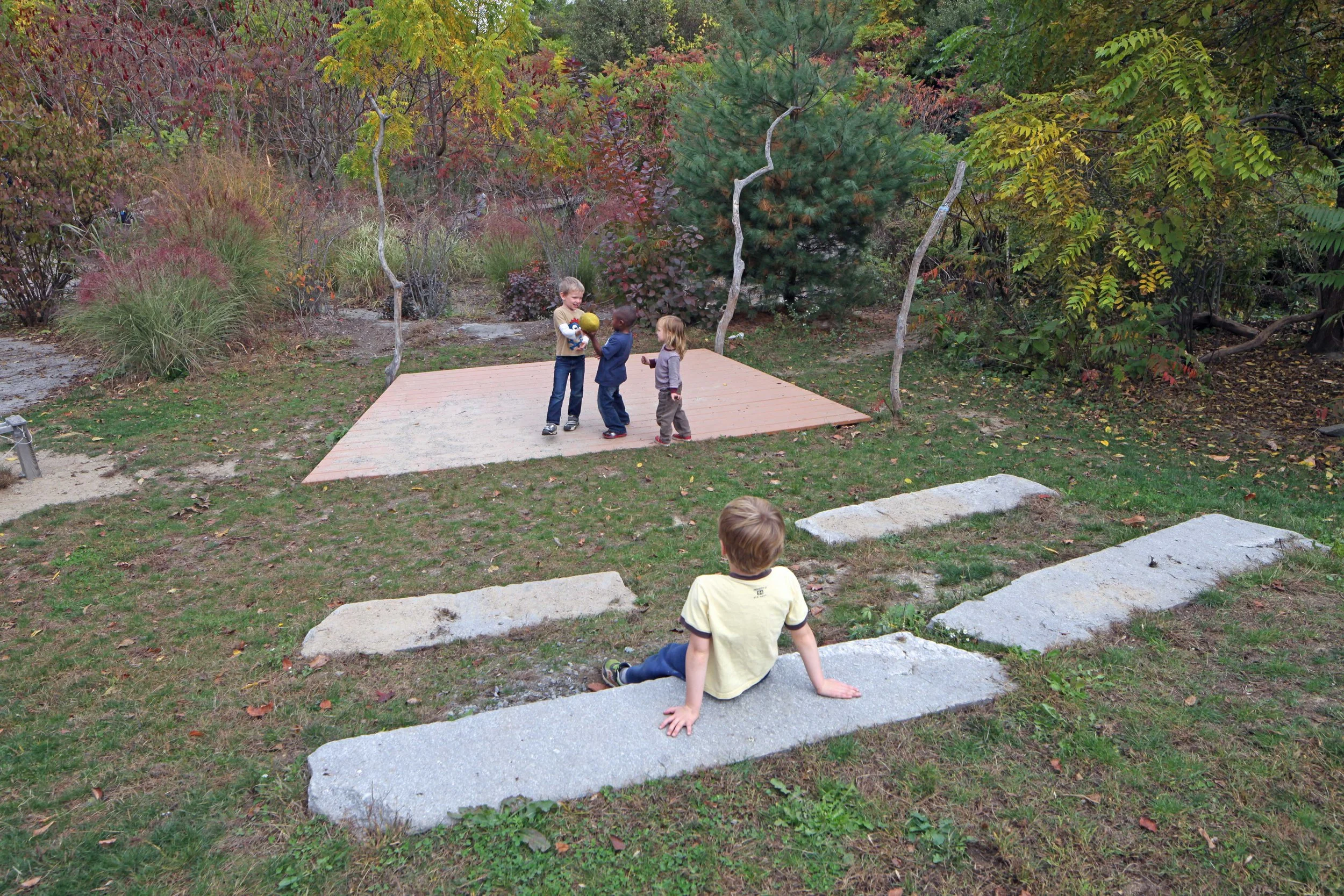 Outdoor performance stage surrounded by natural landscaping, where children gather for imaginative play and activities.