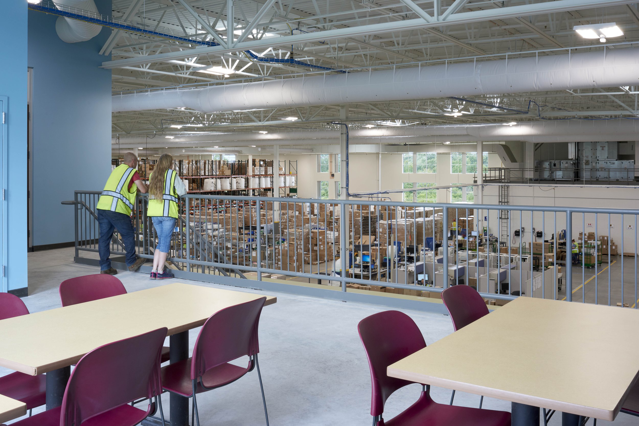 Two people overlook an active warehouse and distribution area from an elevated employee break area.