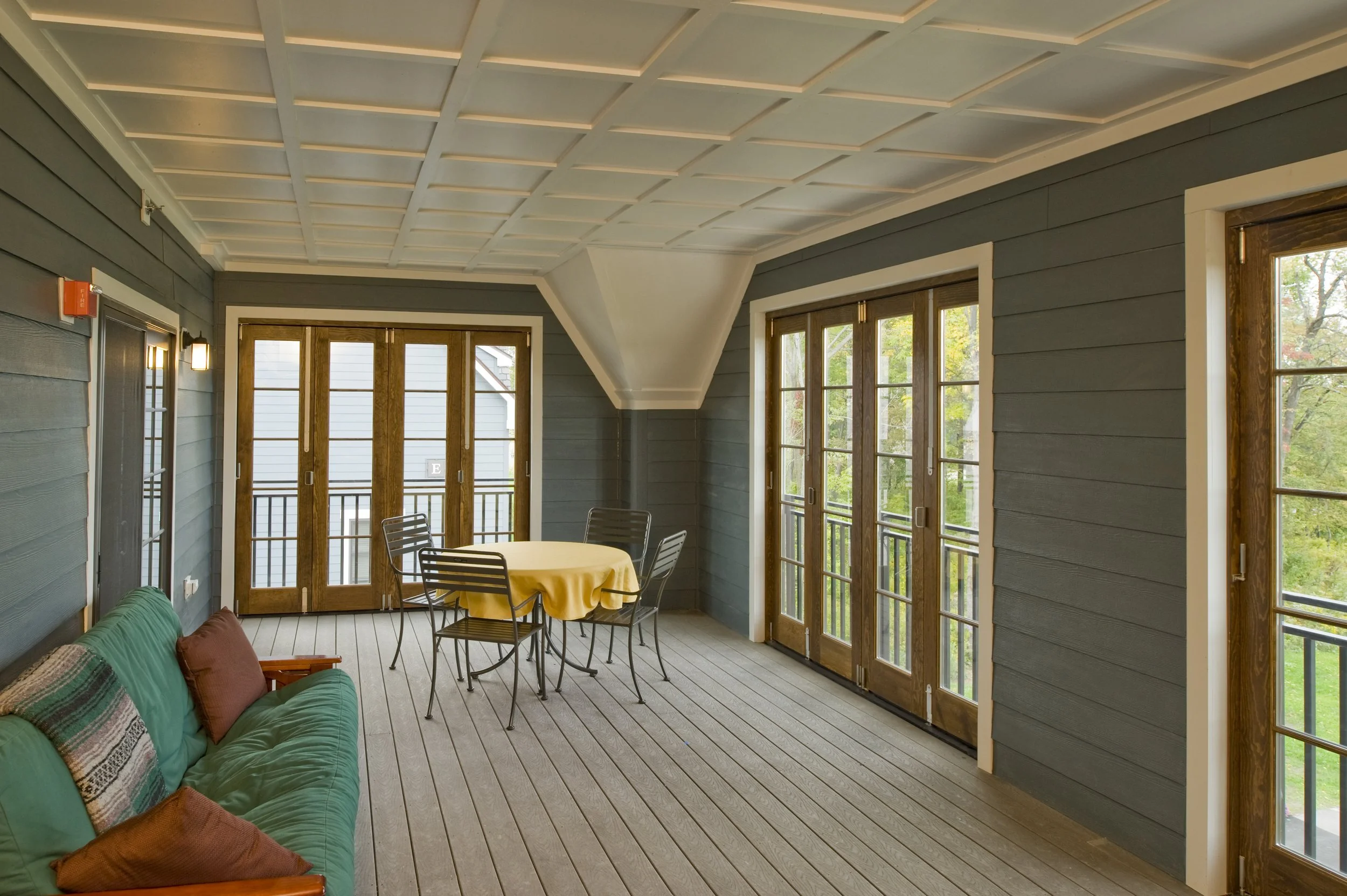 Covered outdoor porch with seating, dining table, and floor-to-ceiling French doors overlooking landscaped grounds.
