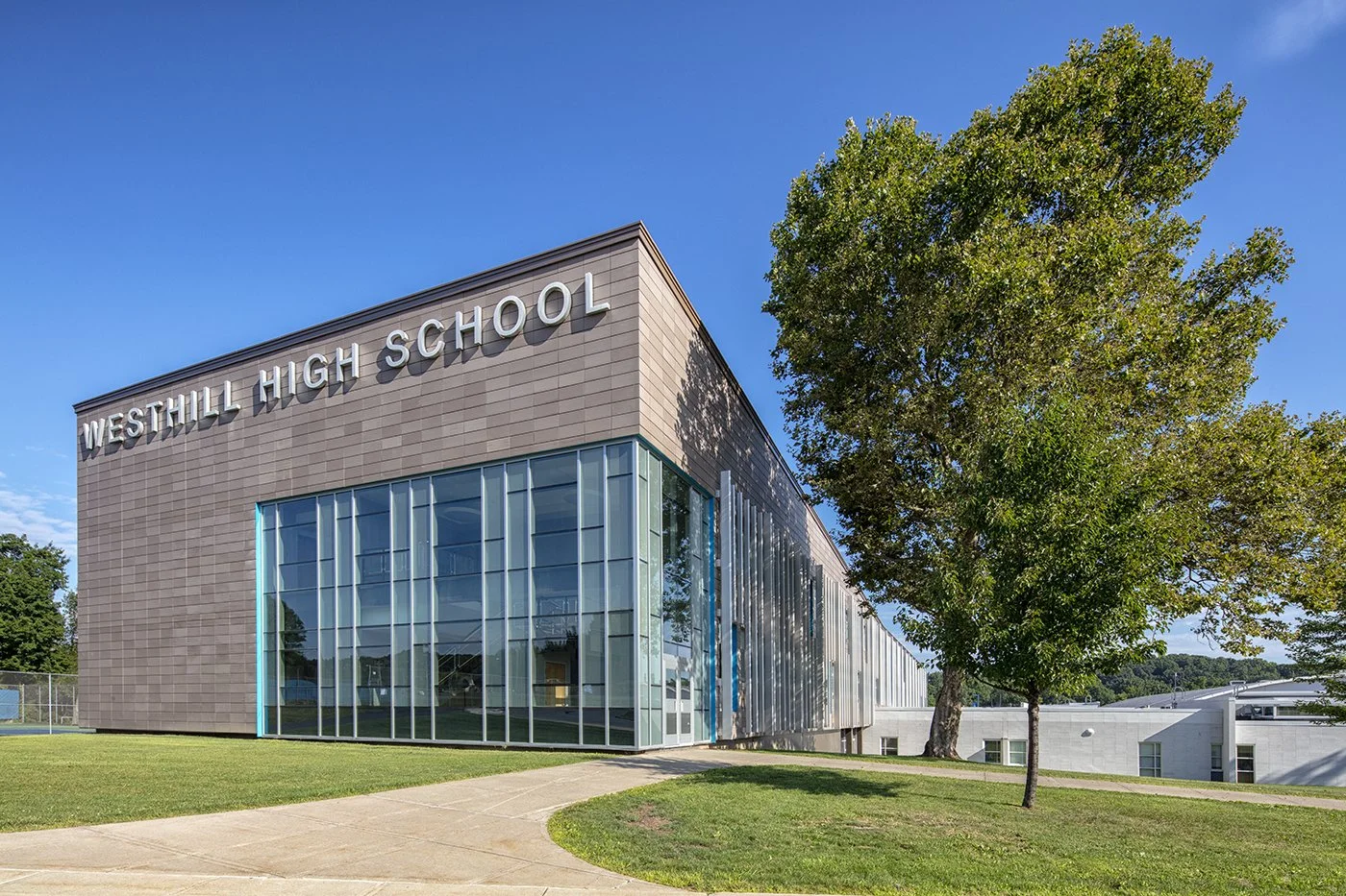 Exterior of Westhill High School featuring a modern facade, expansive glass curtain wall, and landscaped grounds.