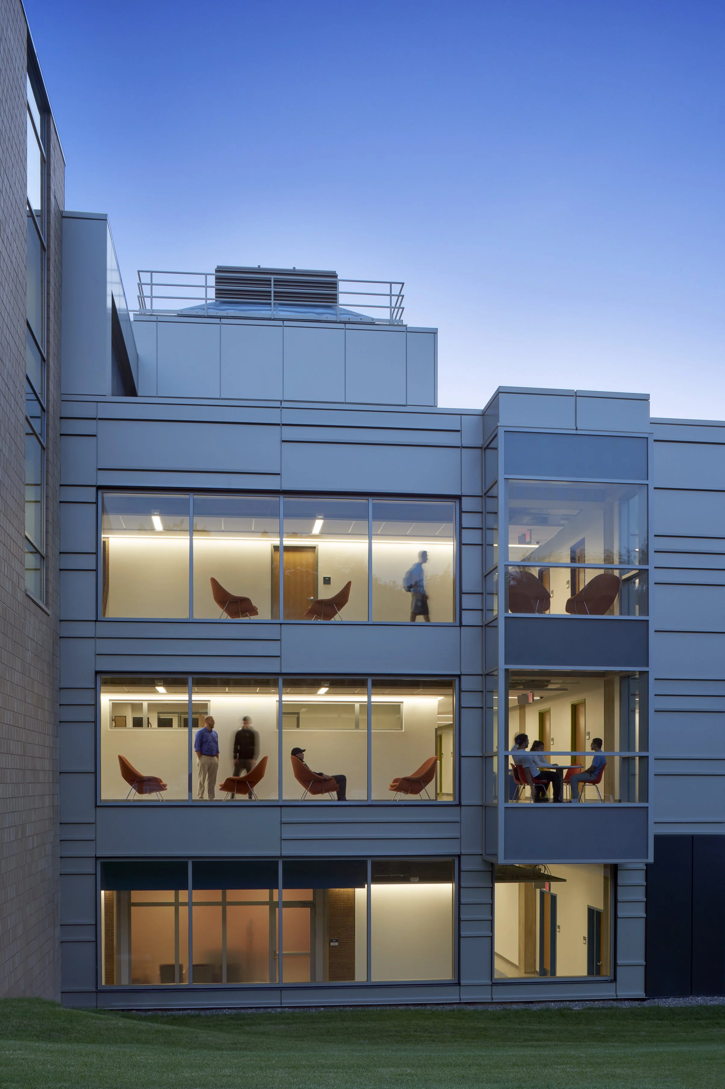 Evening exterior view of the renovated science building, highlighting illuminated student gathering and collaboration spaces through expansive windows.