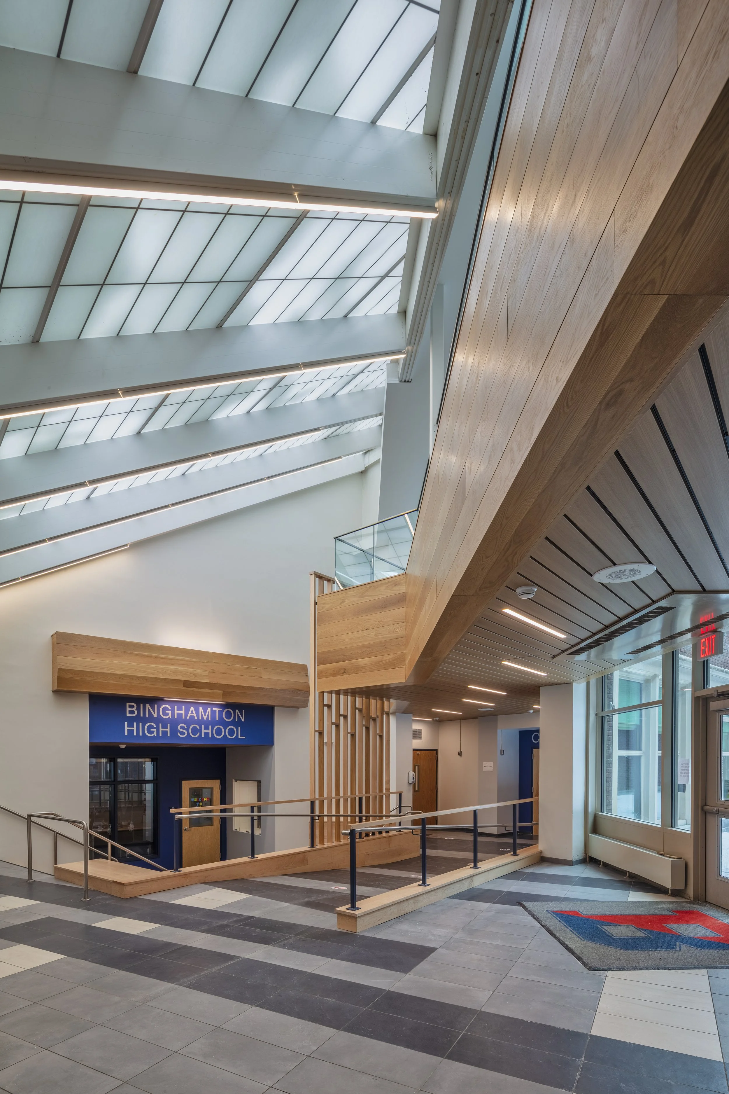 Renovated Binghamton High School entrance atrium featuring a skylit ceiling, wood architectural elements, glass railings, and accessible ramps.