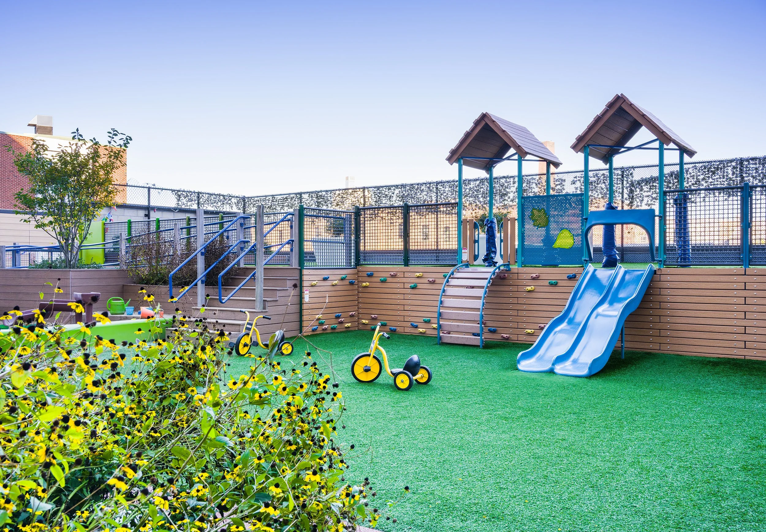 Children’s playground with artificial turf, climbing walls, slides, tricycles, and raised play structures.
