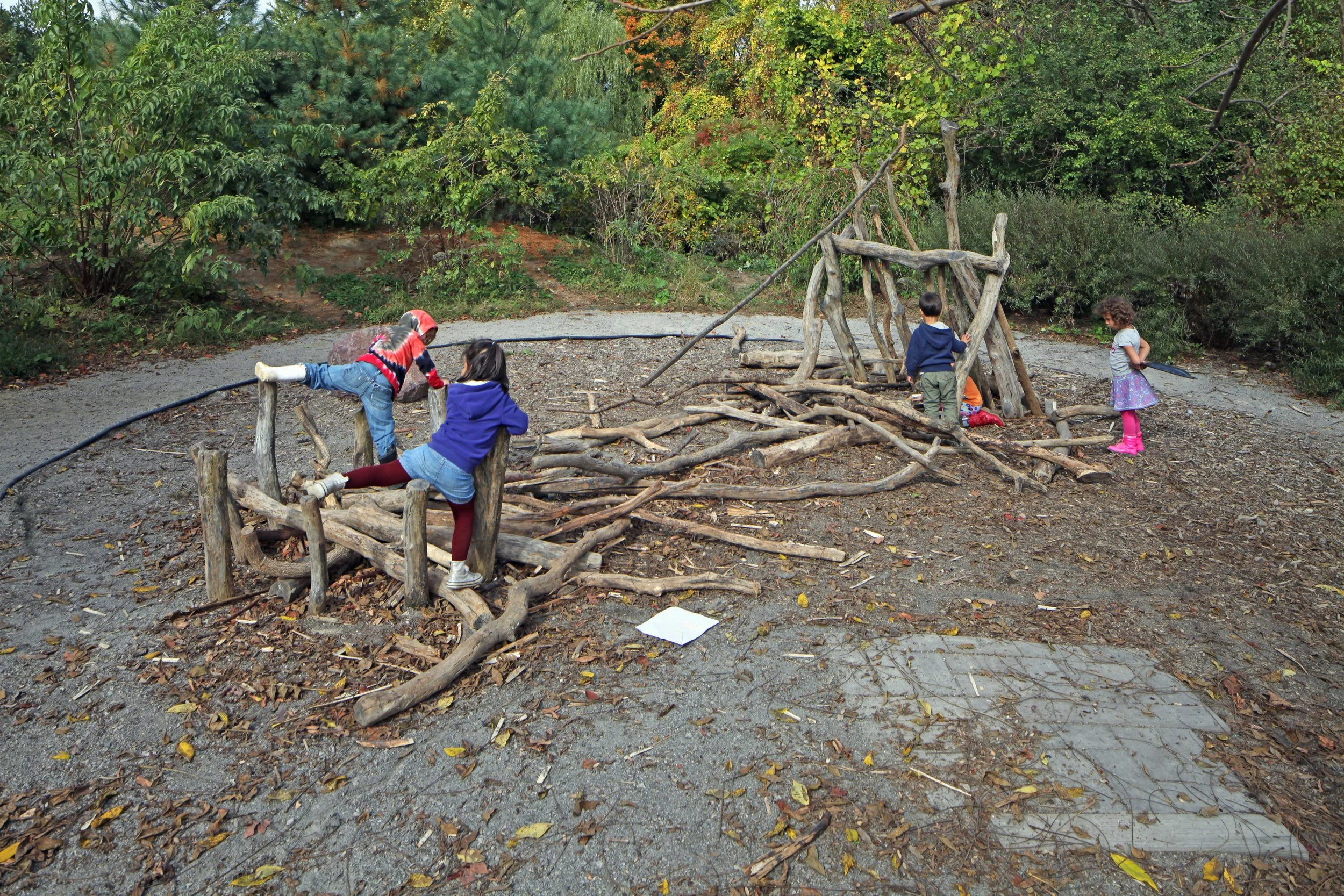 Children use logs, branches, and natural loose parts to build, climb, and create imaginative play structures.
