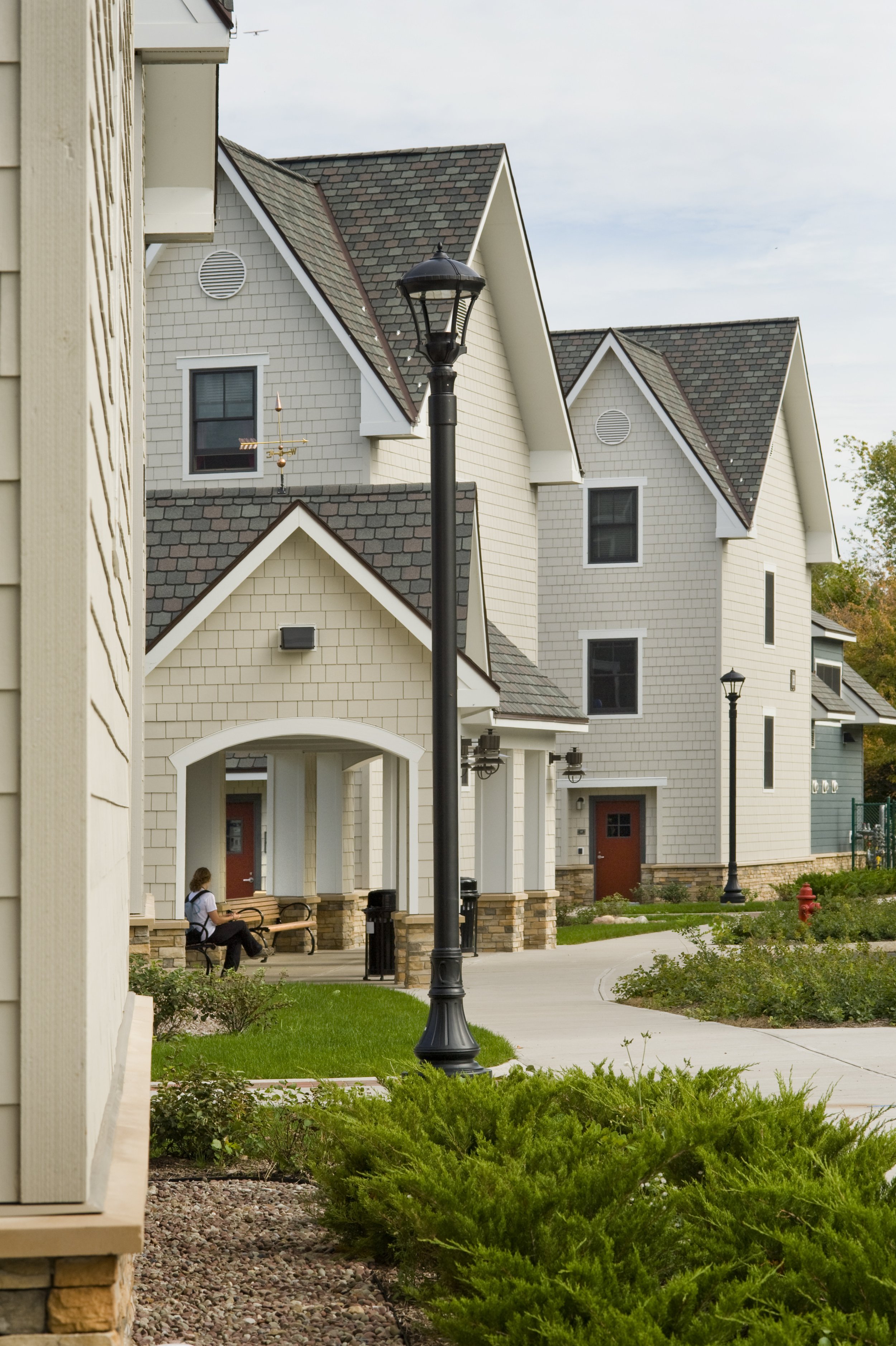 Apartment building entrance featuring covered entryways, landscaped walkways, benches, and decorative street lighting.