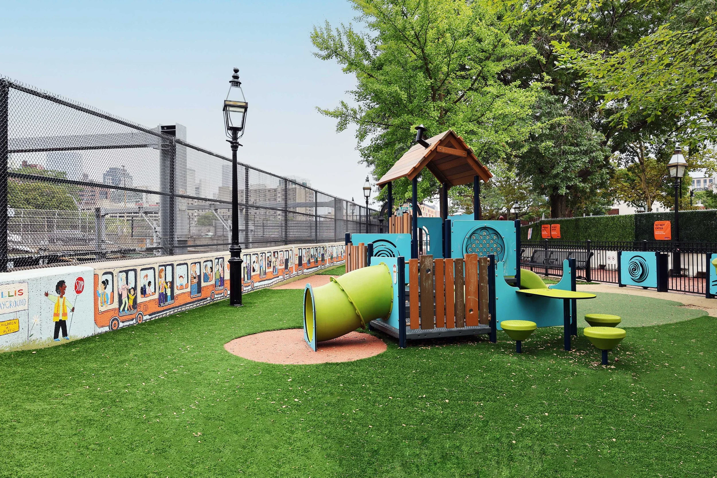 Colorful play structure with slides, tunnels, and activity panels surrounded by artificial turf and mature trees at Ellis Early Learning.