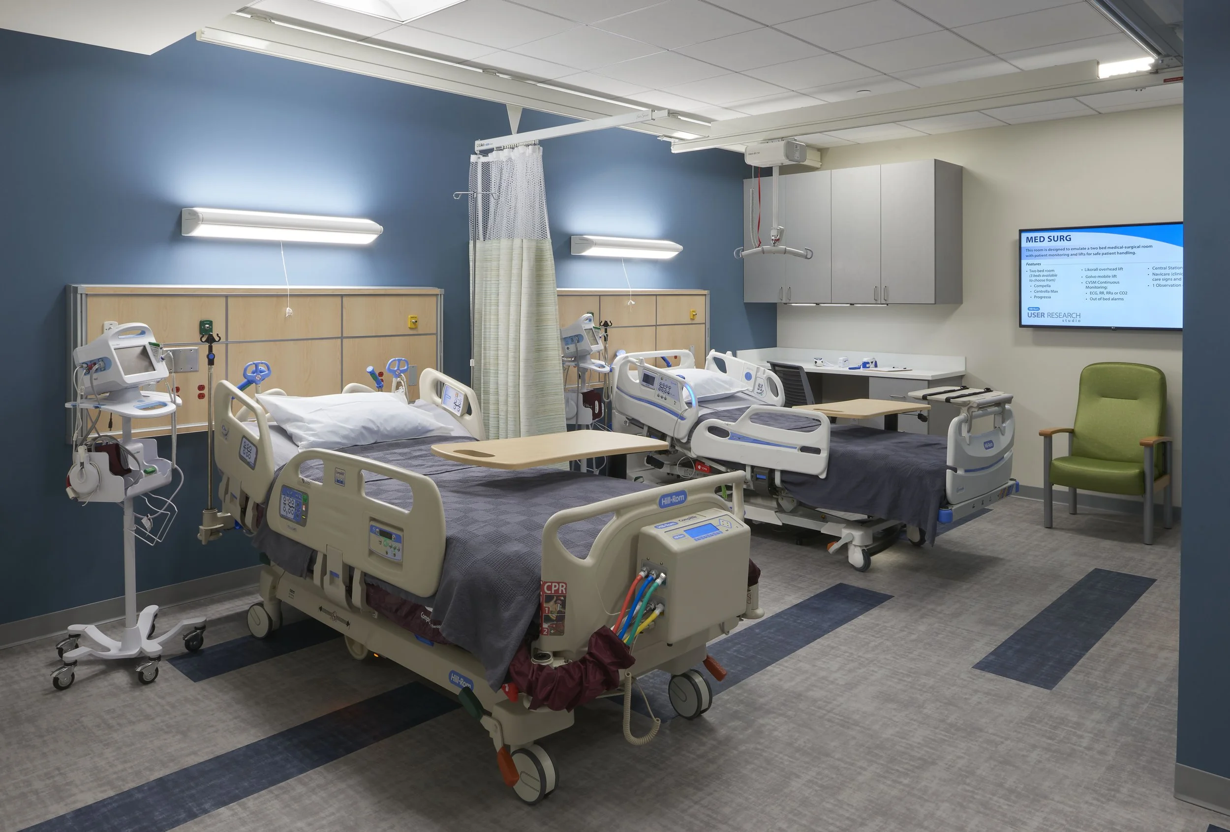 User research space simulating a hospital room with patient beds, medical equipment, privacy curtain, and observation technology.