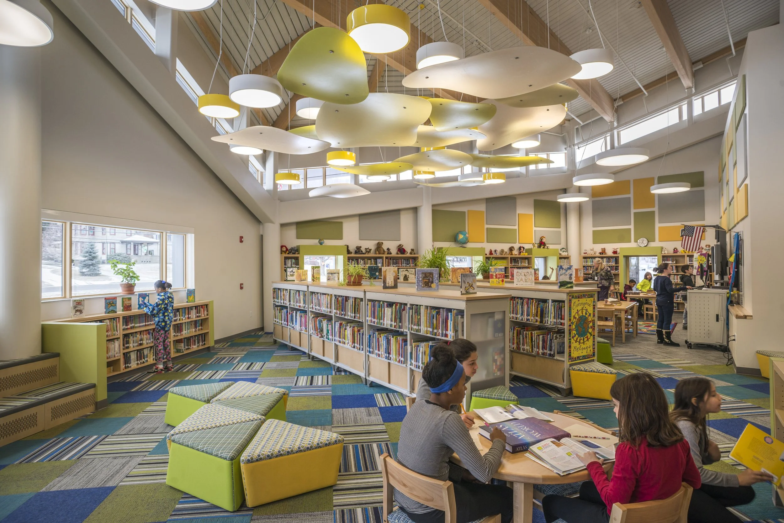 Bright elementary school library with flexible seating, colorful finishes, abundant daylight, and students reading and learning.