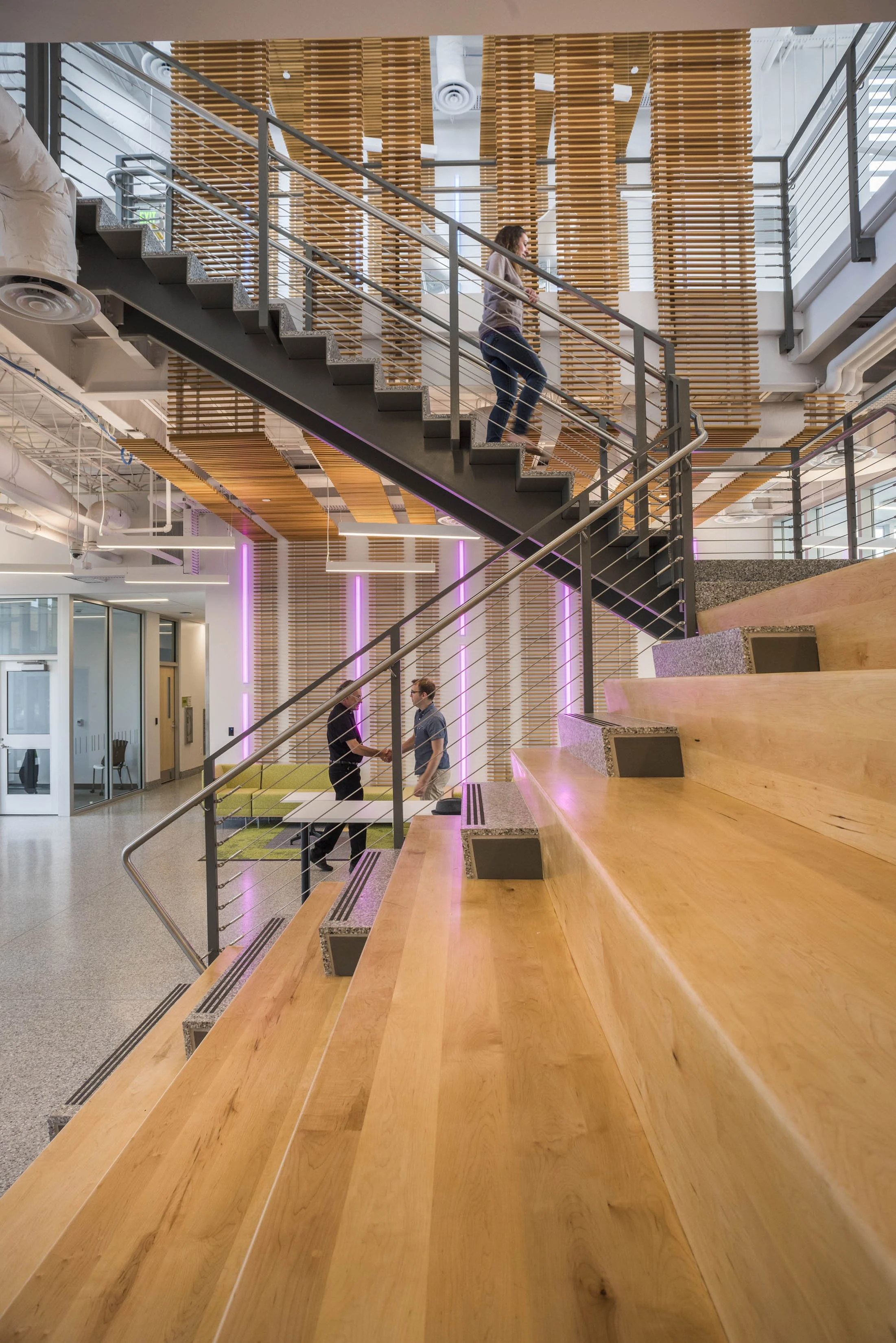 Open central stair with tiered seating, collaborative gathering space, and architectural wood detailing designed to promote interaction between tenants.