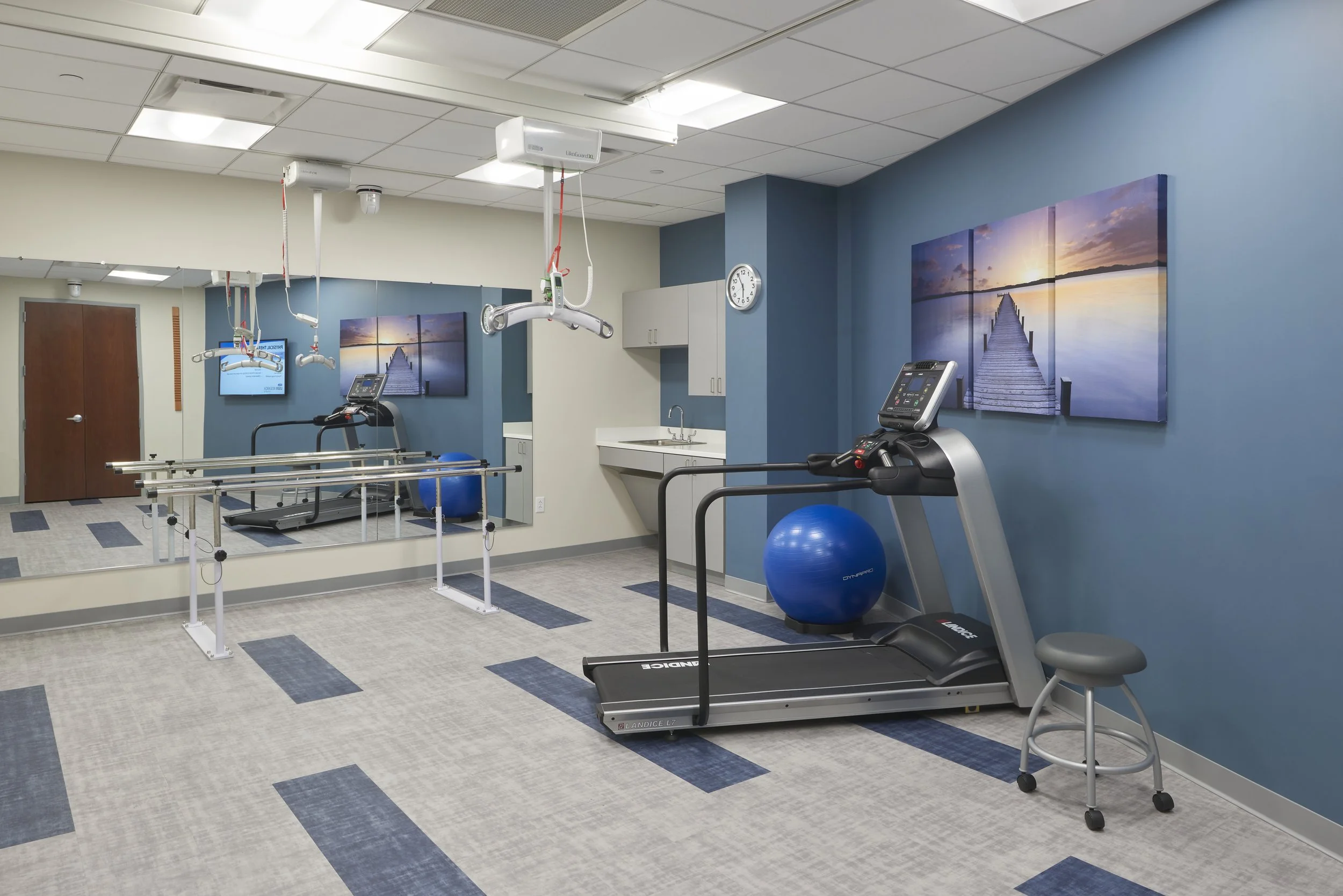 Clinical simulation space with treadmill, parallel bars, patient lift equipment, and other rehabilitation equipment.