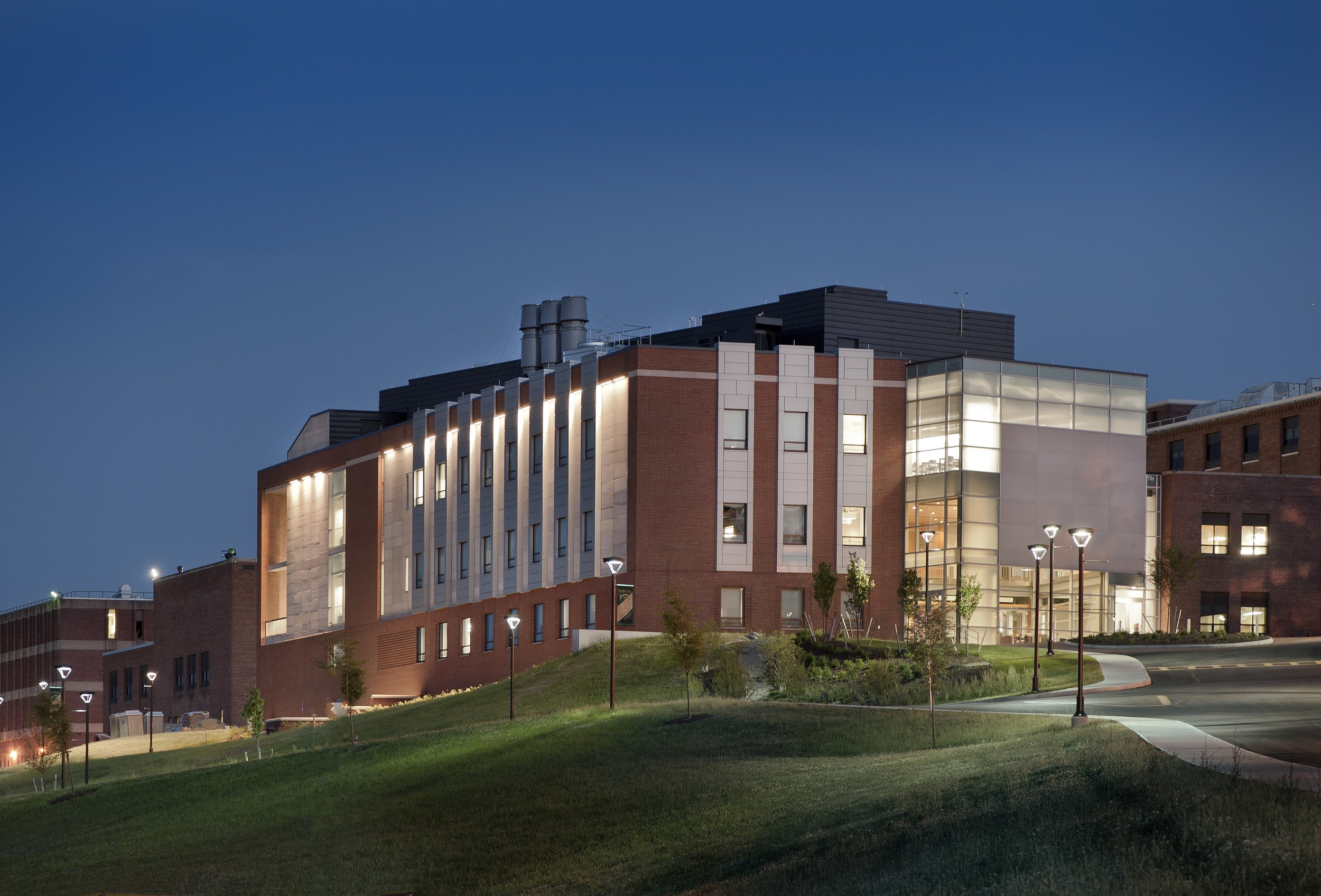 Exterior view of the Le Moyne College Coyne Science Center Addition at dusk, featuring a glass entrance, brick and metal façade, and landscaped campus setting.
