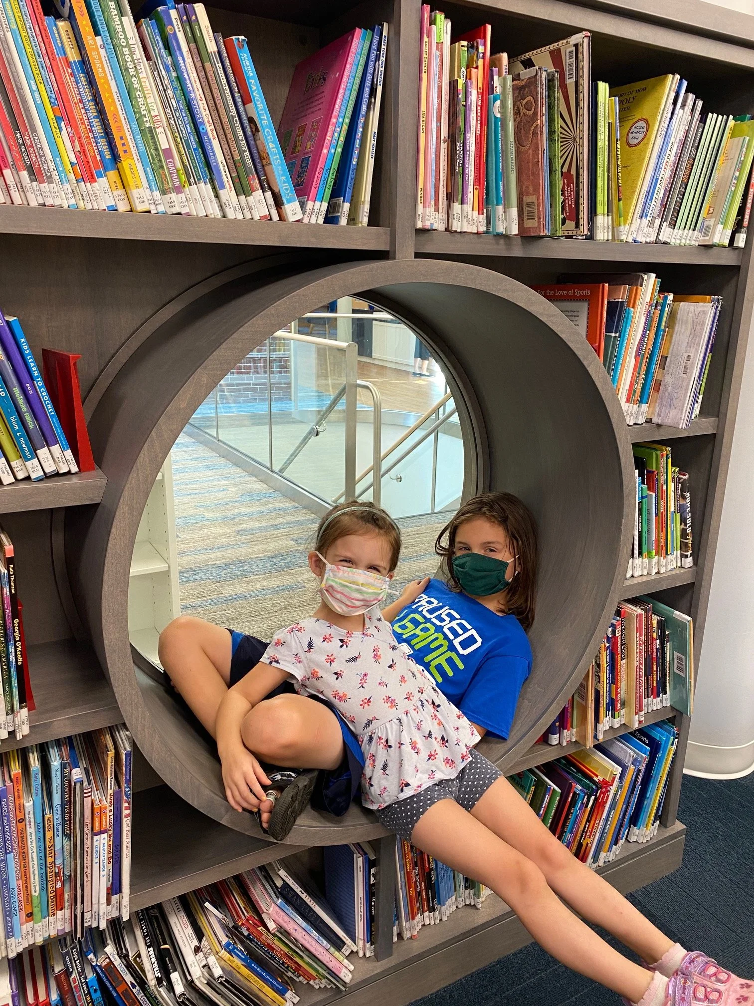 Two children sitting together inside a circular reading nook built into a bookshelf.