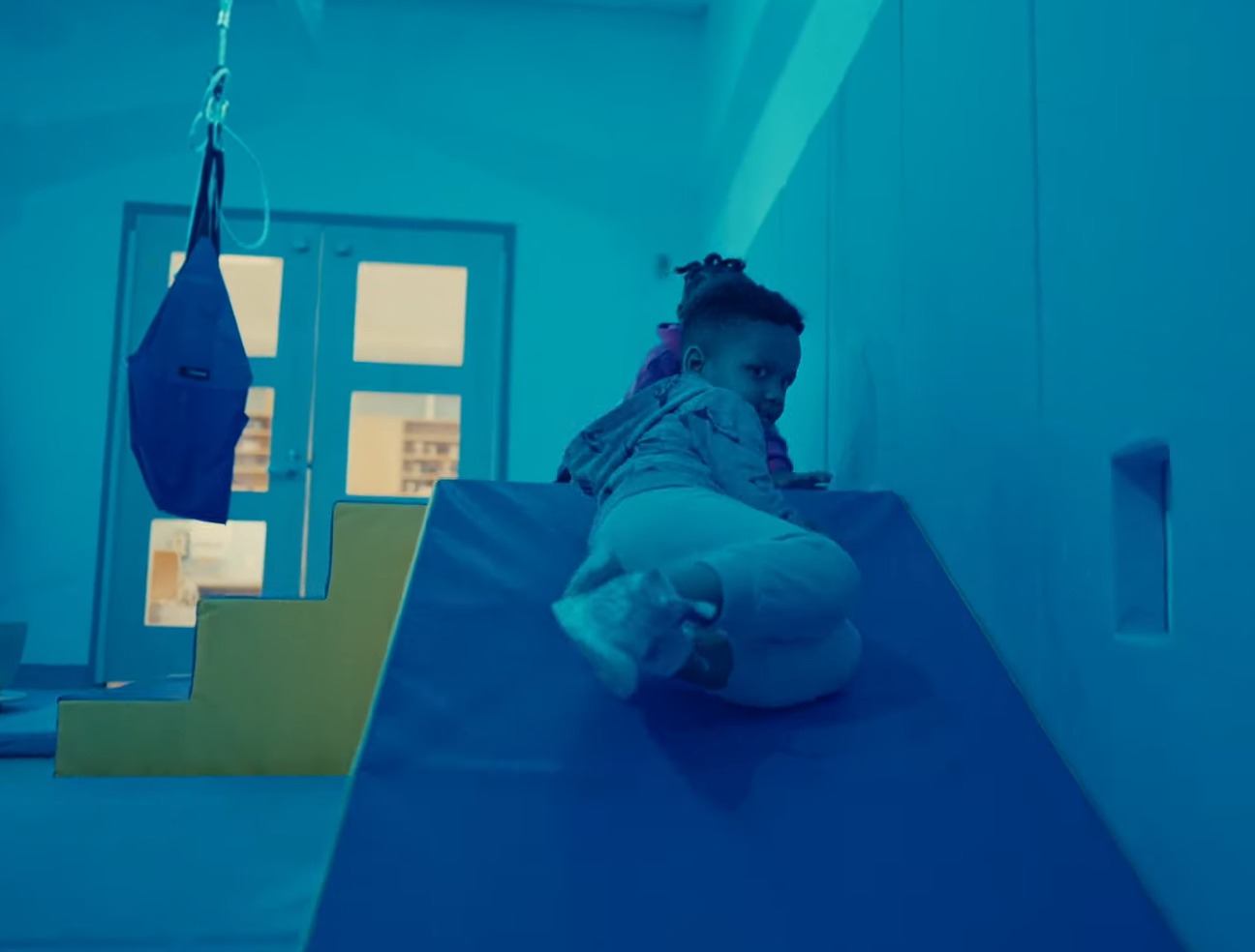 A child climbs and slides on soft play equipment in a sensory gross motor room that encourages active movement, balance, and motor skill development.