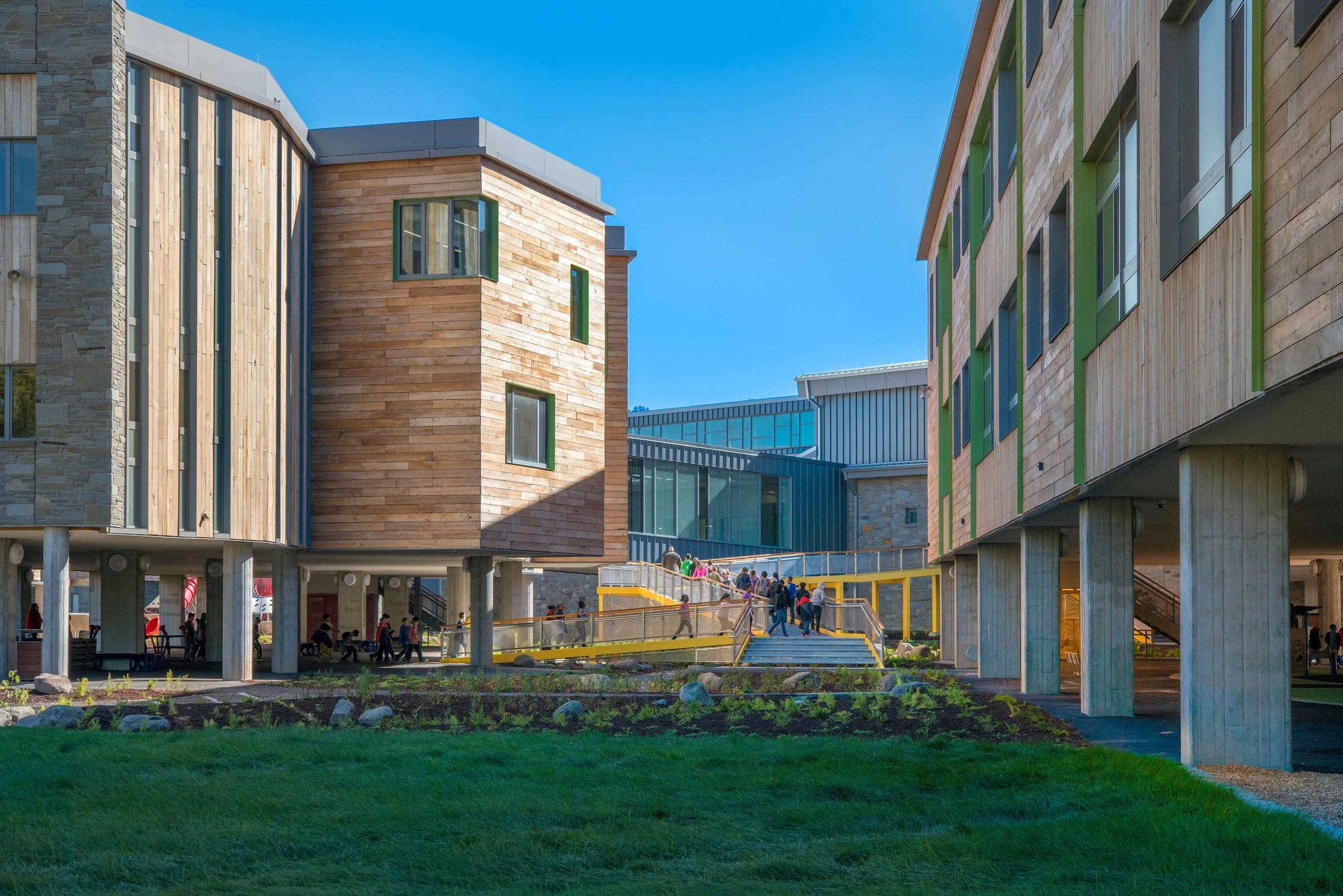 Exterior view between raised classroom wings with students moving through landscaped outdoor learning spaces.