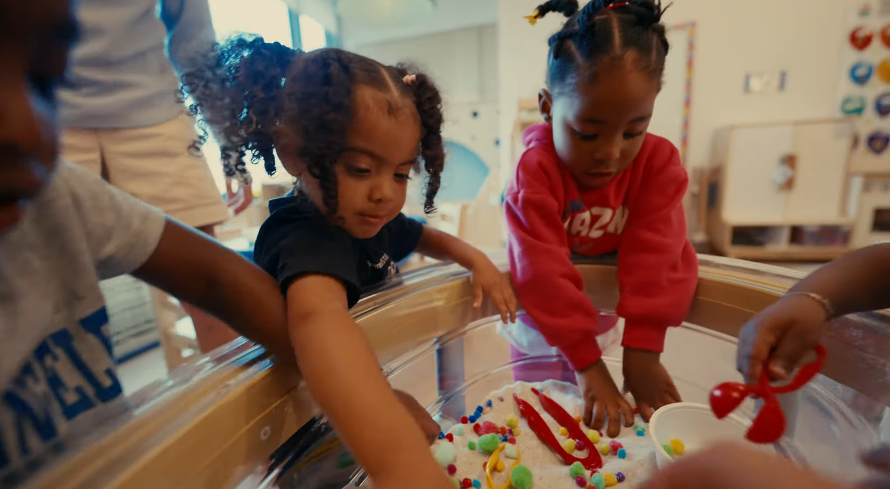 Preschool children gather around a sensory table, exploring textured materials together through hands-on, collaborative play in a bright classroom.
