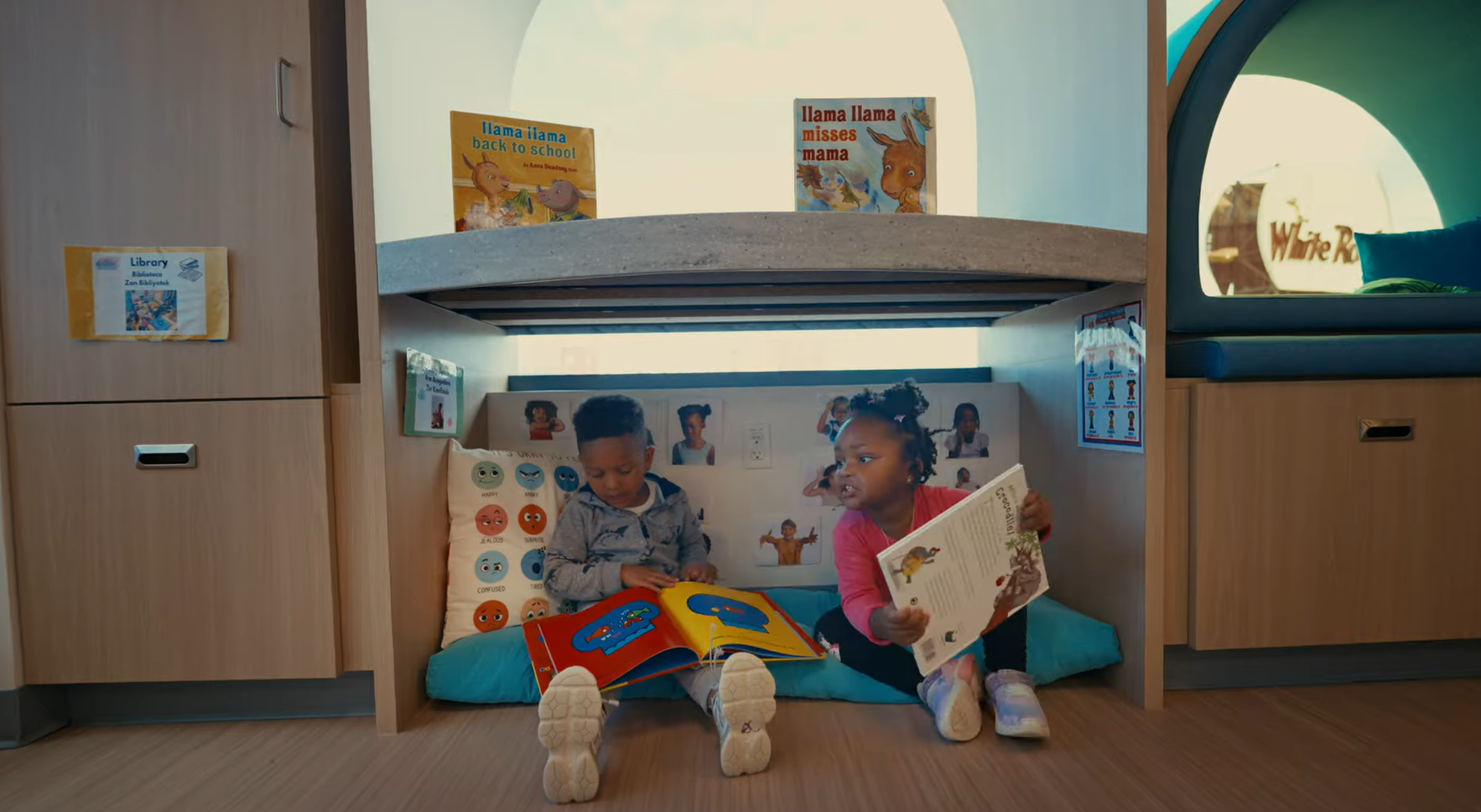 Two preschool children sit in a built-in classroom nook, reading books in a cozy, semi-enclosed space designed to encourage quiet play and self-regulation.