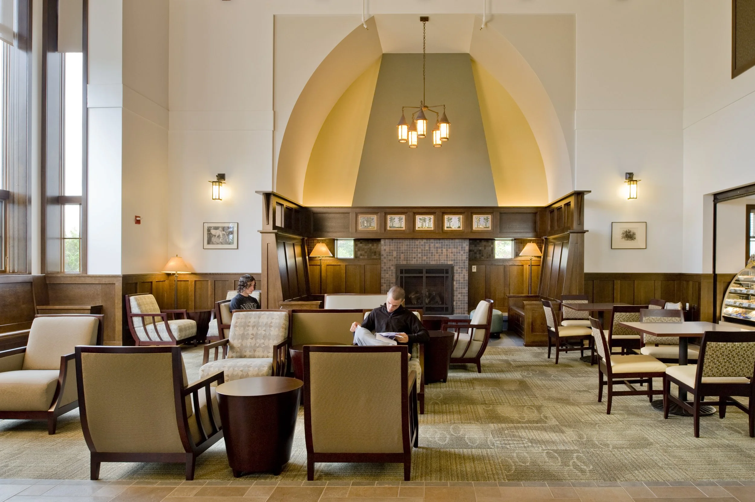 Community lounge with fireplace, comfortable seating, café tables, and vaulted ceilings designed for gathering and relaxation.