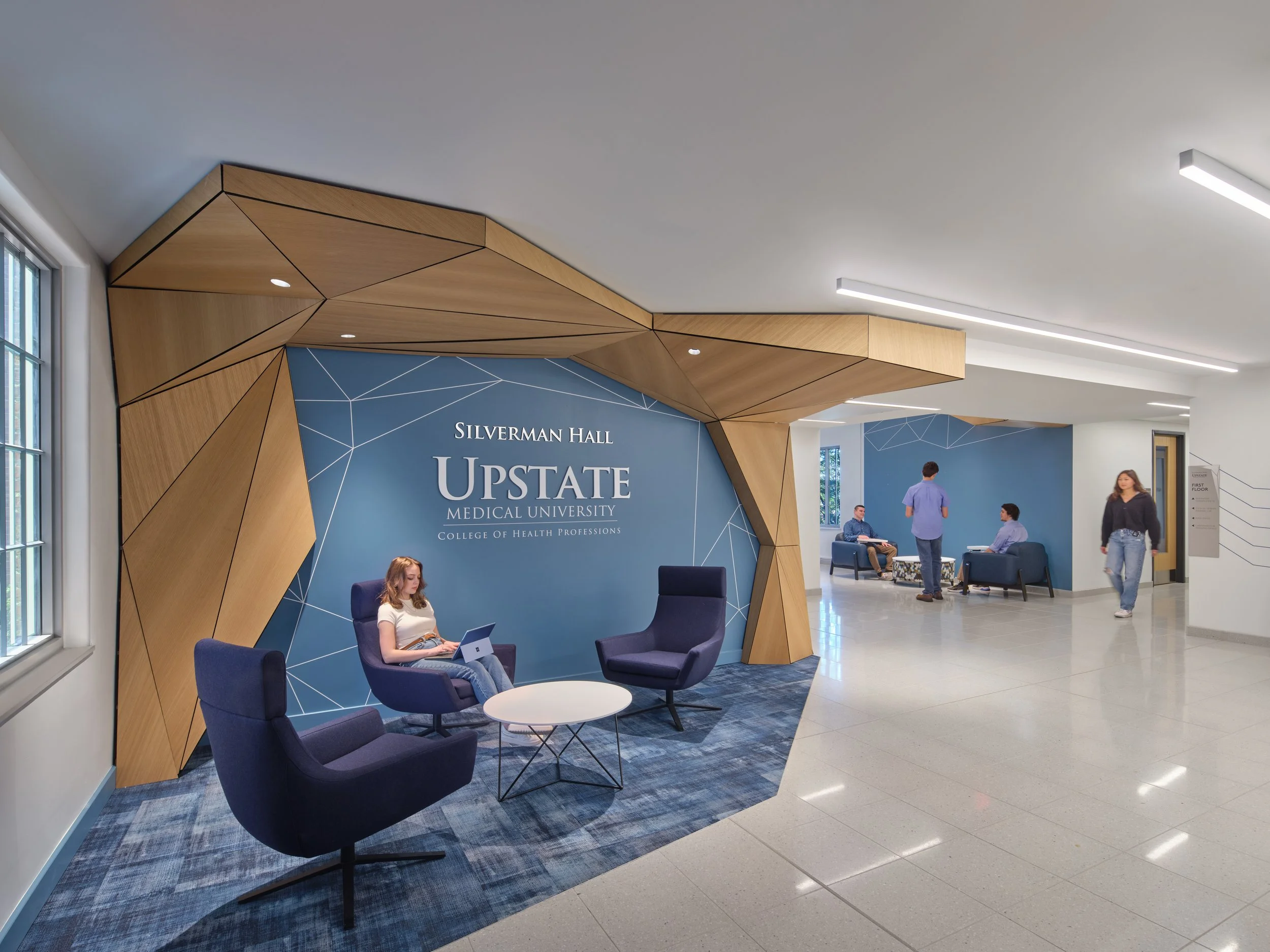 Student lounge area at SUNY Upstate Medical University's Silverman Hall featuring geometric wood ceiling details, comfortable seating, and collaborative gathering spaces.