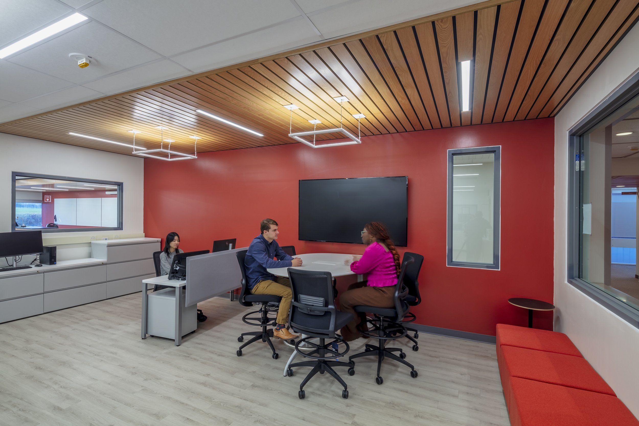 Collaborative learning space with integrated technology, group seating, and red and wood accents.