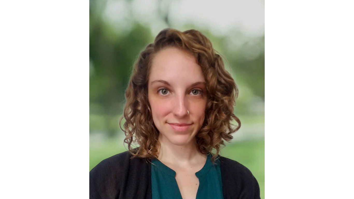 Professional headshot of a woman with curly shoulder-length hair, wearing a dark cardigan over a green top, posed against a softly blurred background.