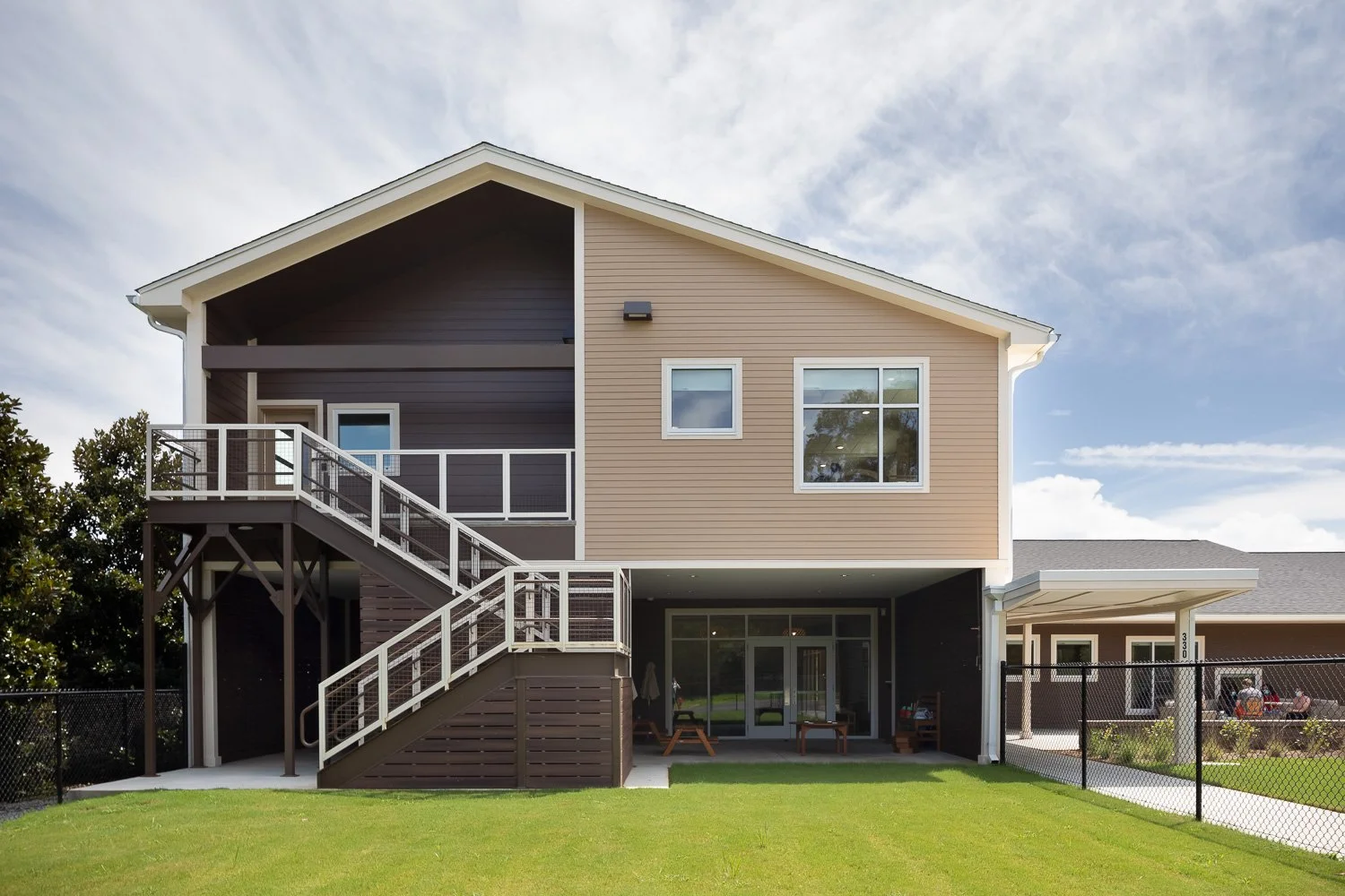 Exterior of a two-story early learning center with covered outdoor areas, an exterior staircase, lawn, and fenced play space.