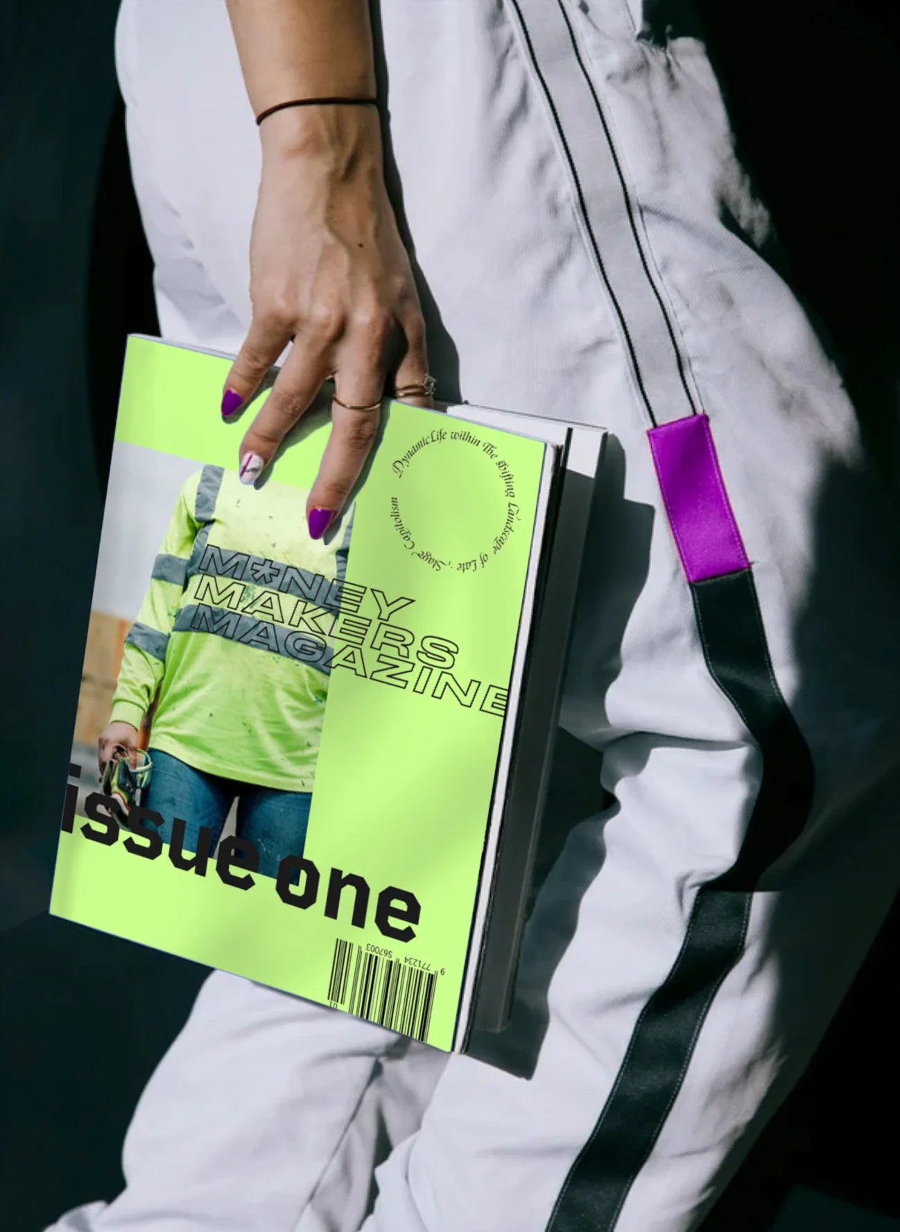 Person holding a magazine titled 'Issue One' with a green cover, featuring a person in a neon green shirt on the cover. The person is wearing white pants with black stripes and has painted nails.
