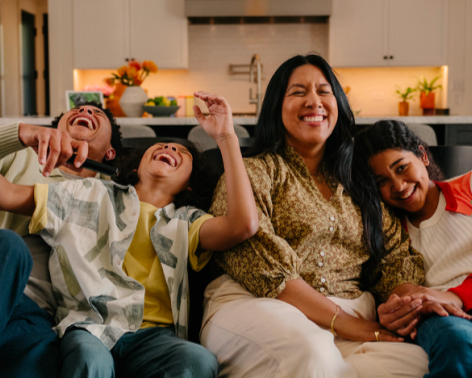 A woman and two children sitting on a sofa, laughing and enjoying each other's company in a modern kitchen.