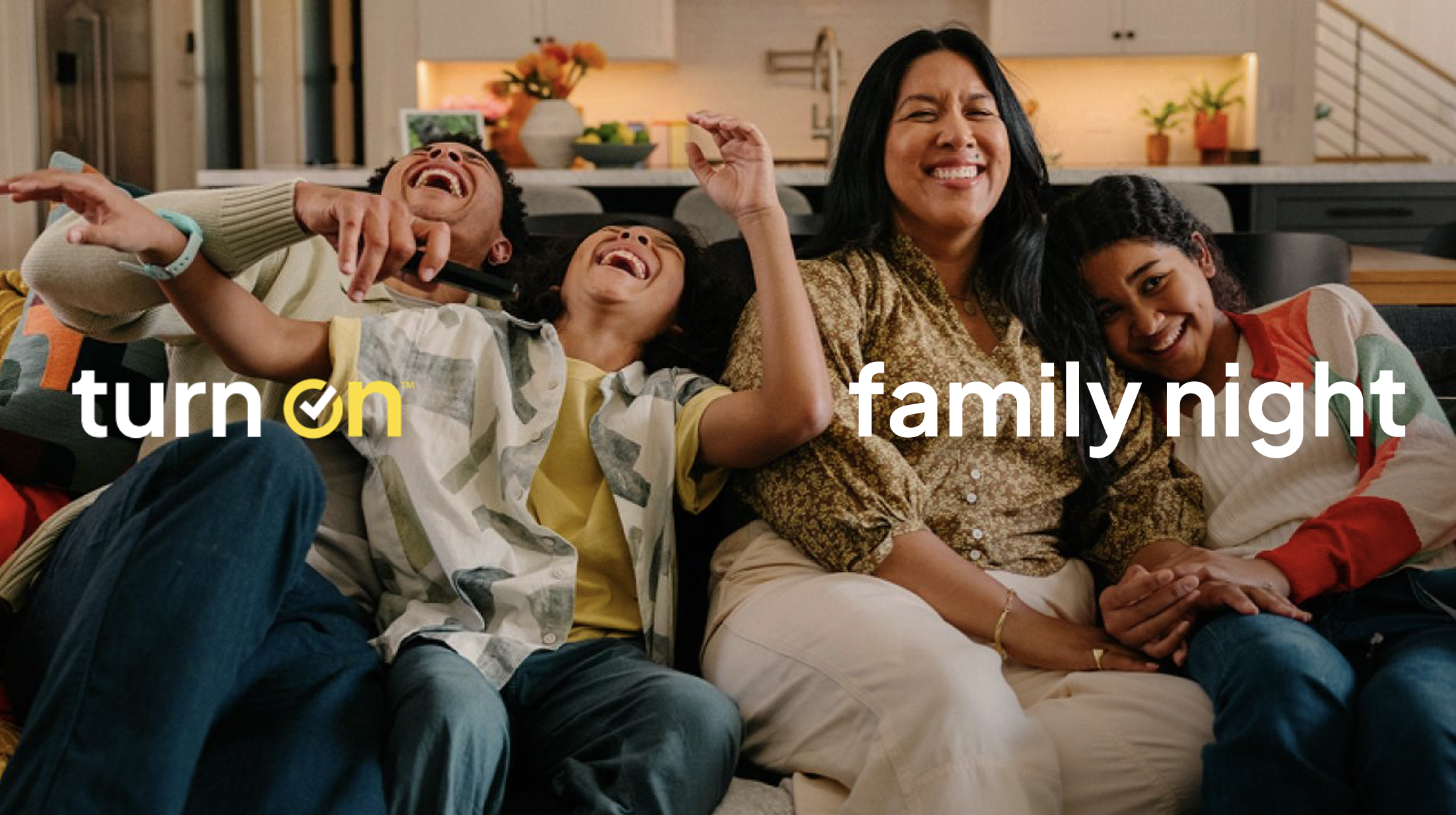 A family of four laughing and enjoying each other's company on a couch in a cozy, brightly lit living room during family night.